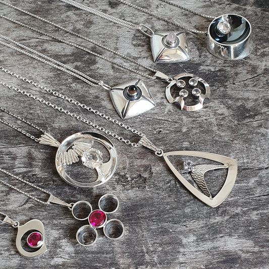 Collection of silver jewelry pieces including necklaces, pendants, and rings with gemstone accents.