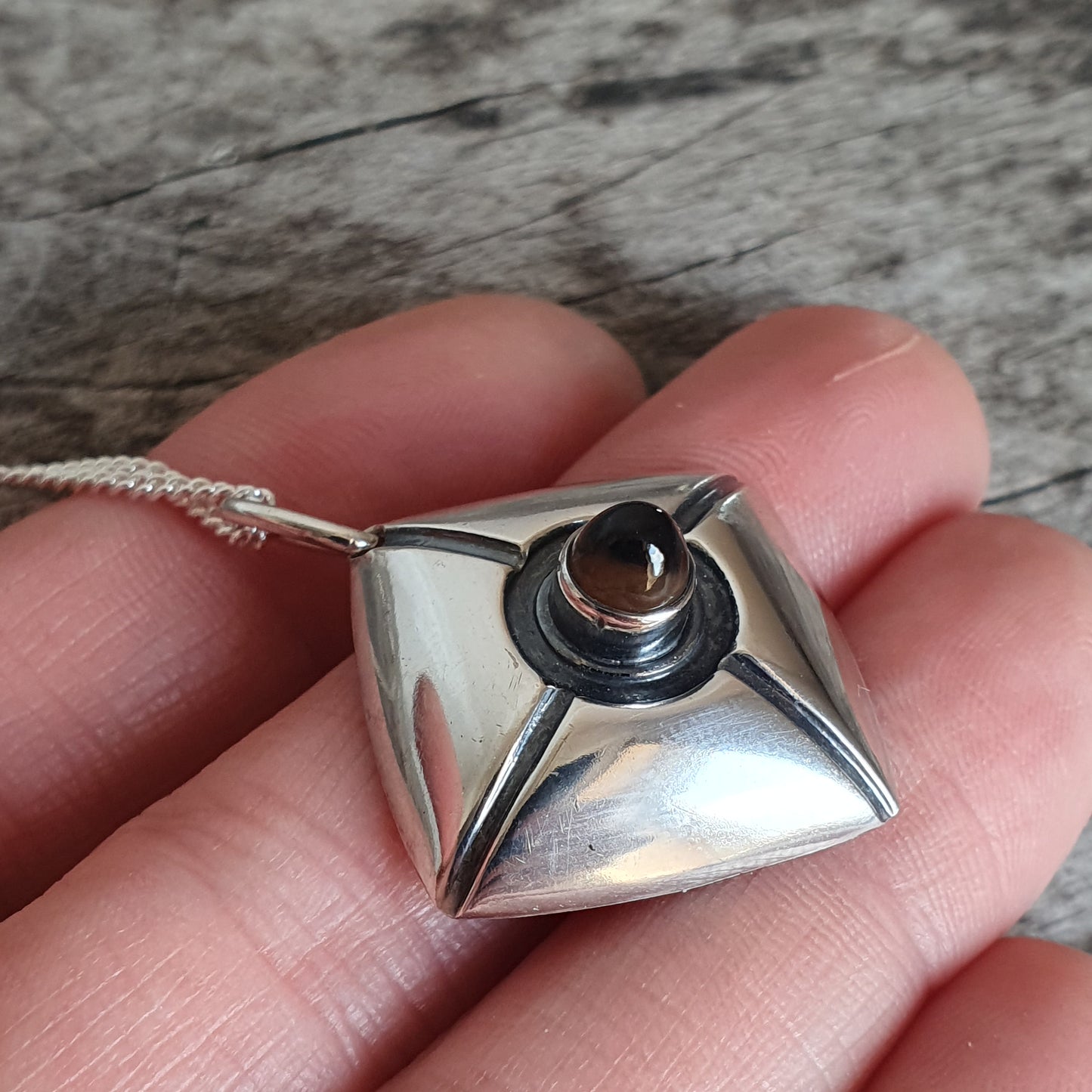 Silver pyramid-shaped pendant with a circular opening at its apex.