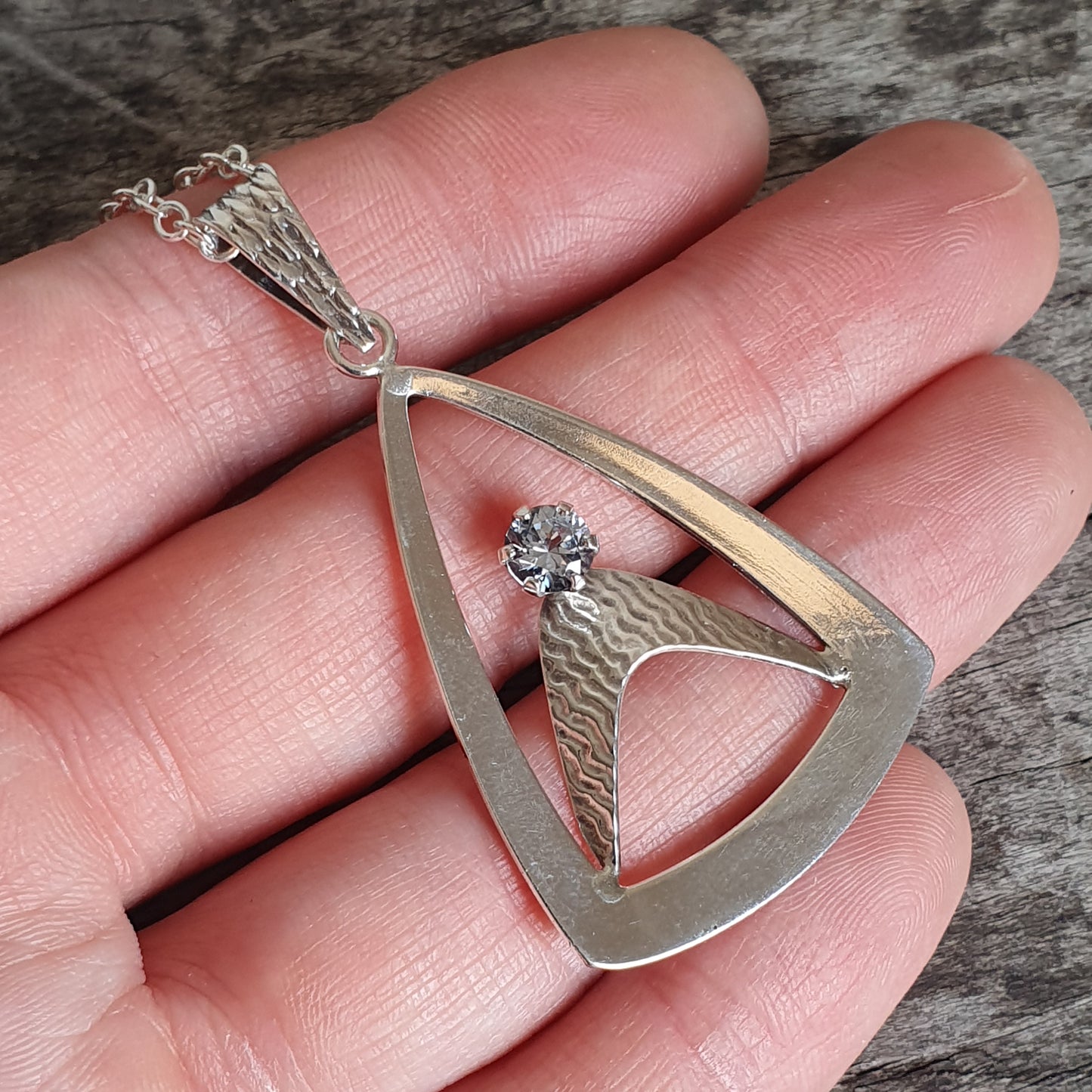 Silver pendant necklace with a triangular design and a small gemstone.