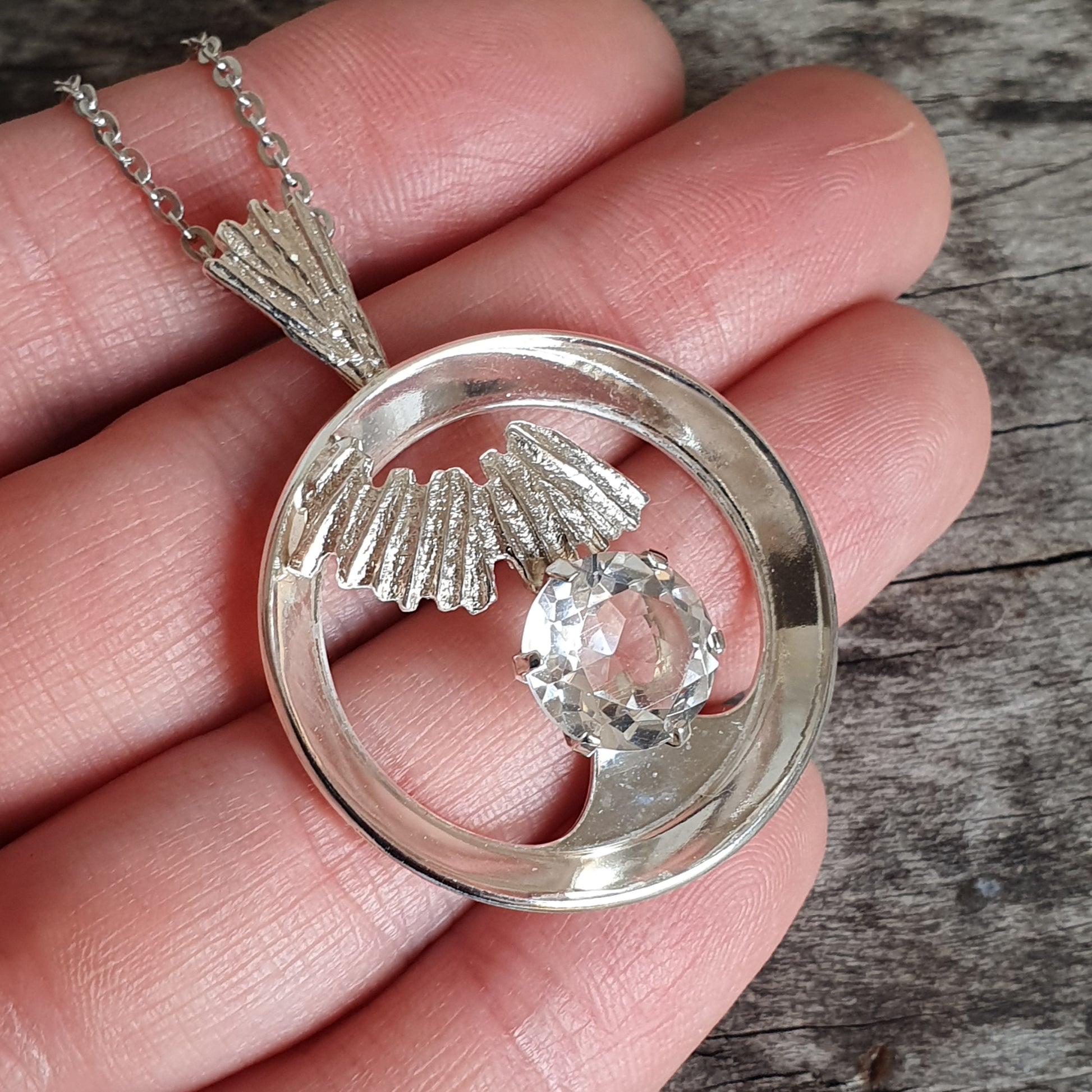 Silver pendant necklace featuring a circular design with a wing motif and a clear gemstone.