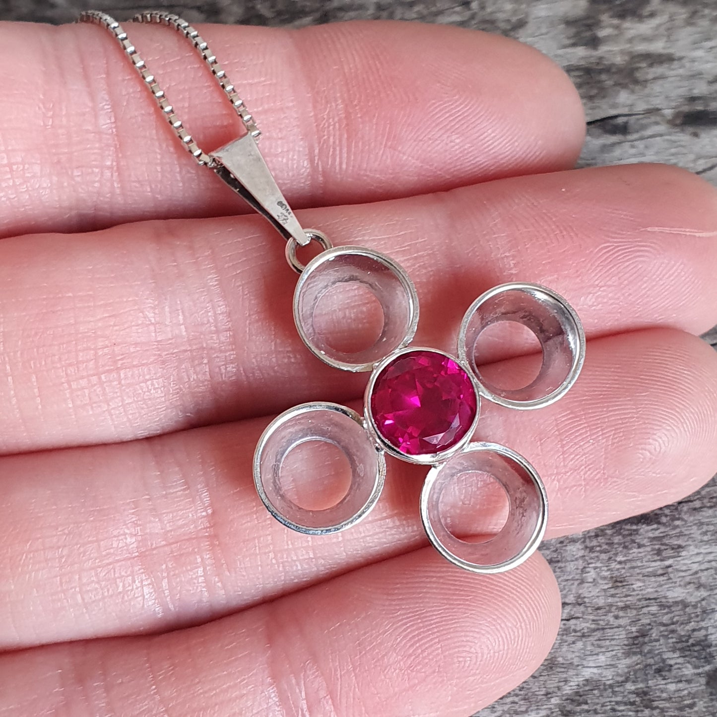 Silver pendant necklace with a cross-shaped design featuring a central pink gemstone and four circular openings.