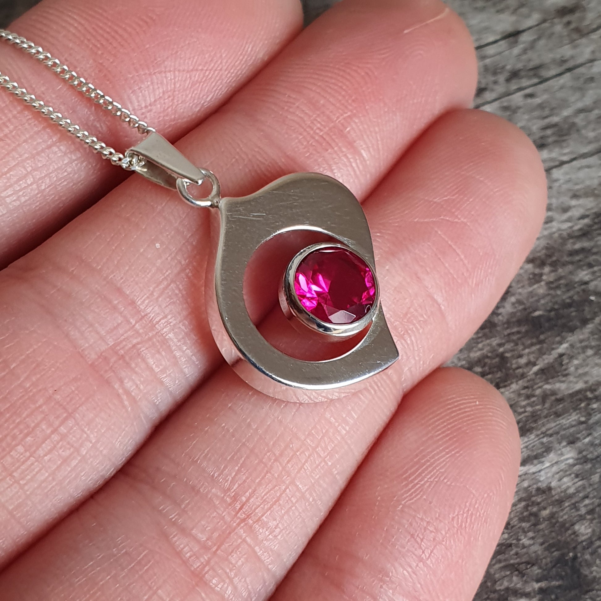 Silver pendant necklace with a curved design and a pink gemstone.