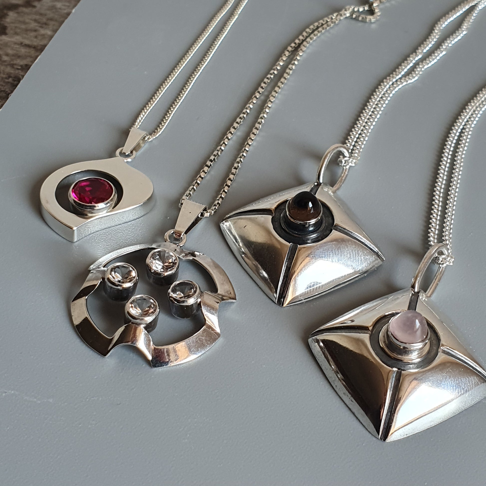 Collection of silver pendant necklaces with geometric designs and gemstone accents.