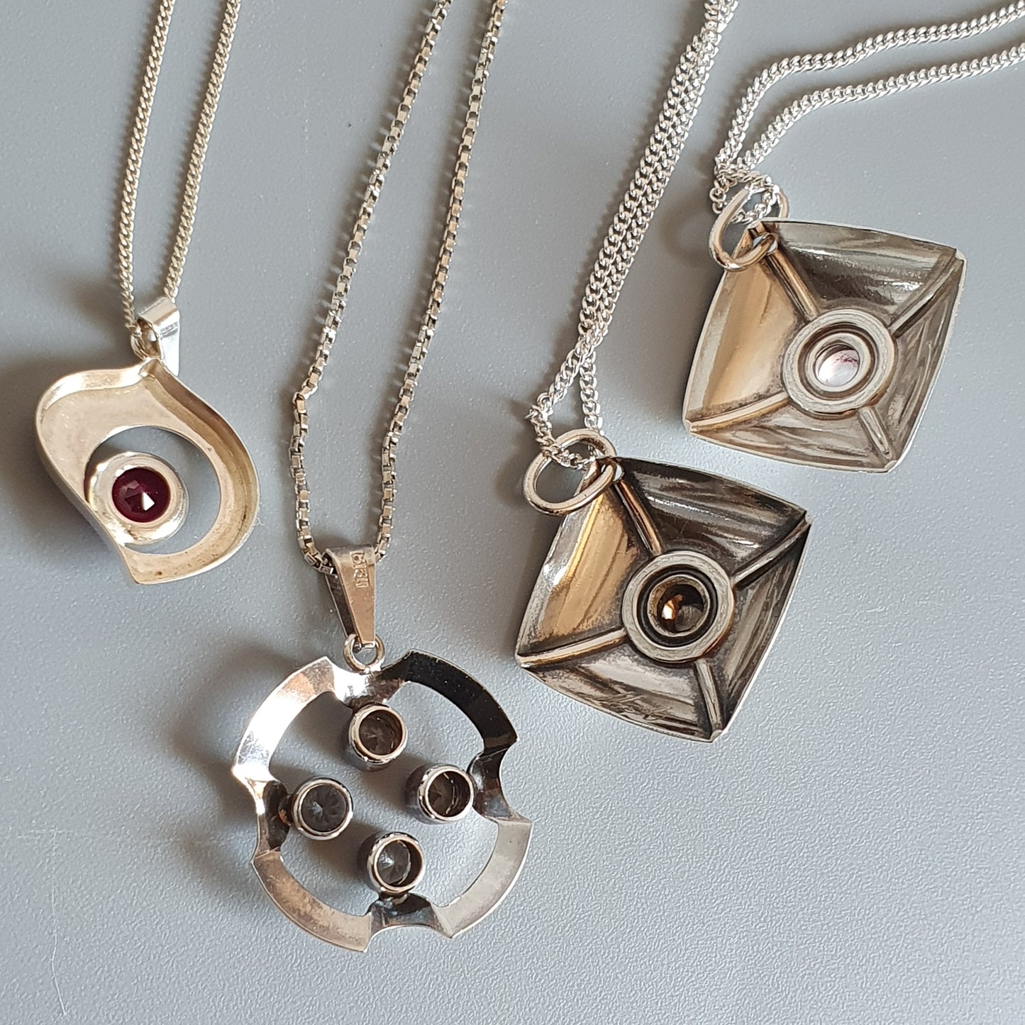 Collection of silver pendant necklaces with geometric and eye-like designs.