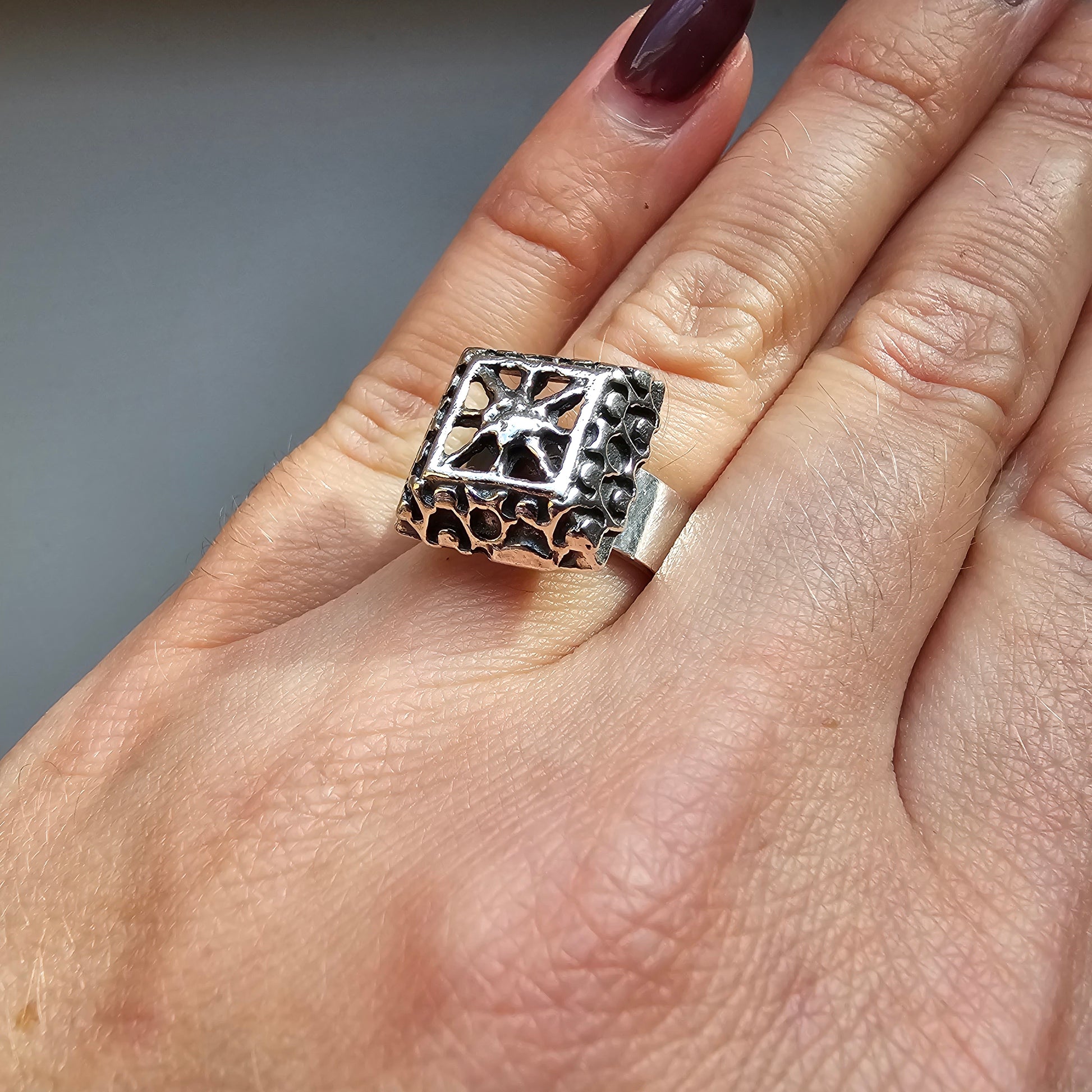 Ornate silver ring with a square top featuring a star-like design and intricate metalwork.