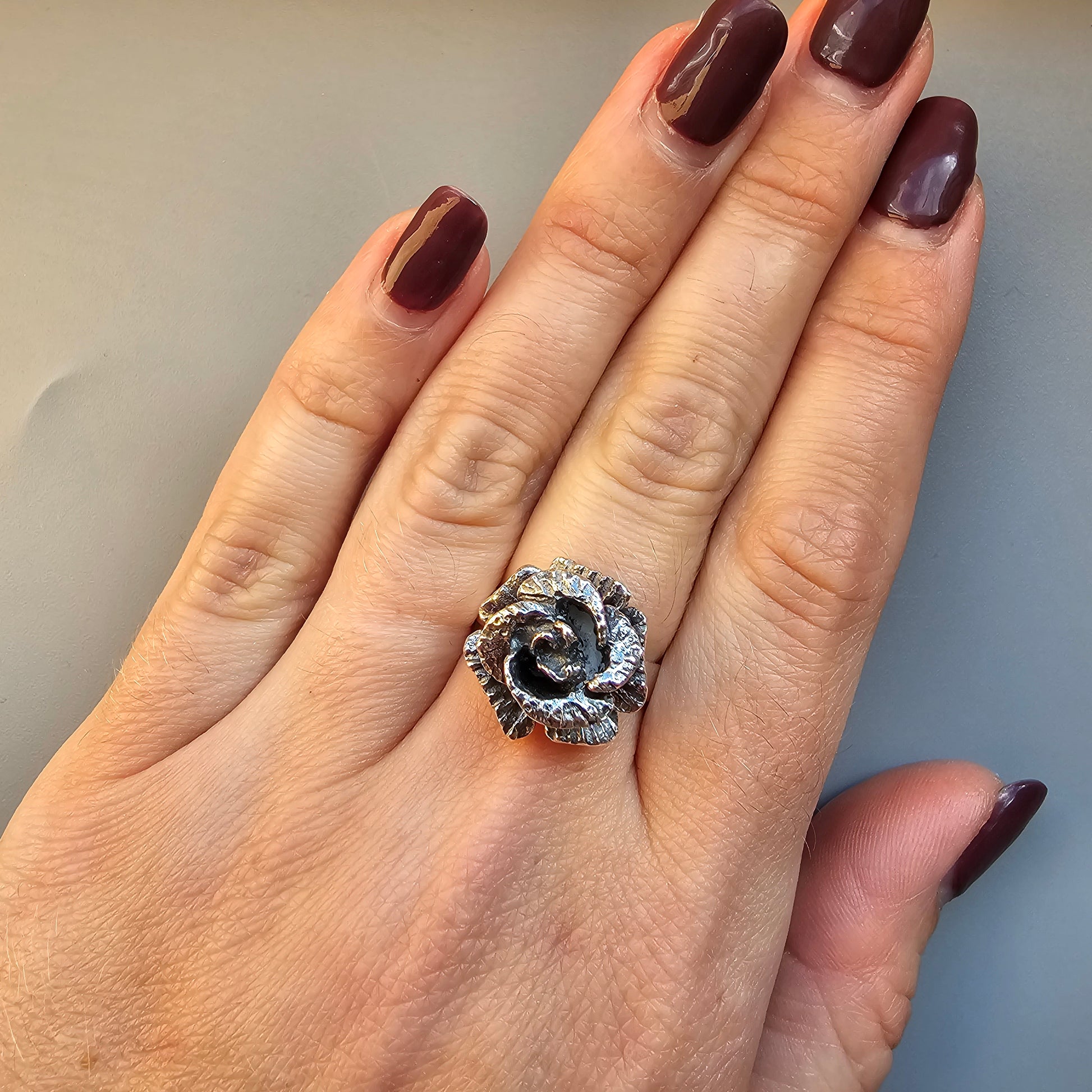 Ornate silver ring with a spiral design and gemstone accents worn on a finger.