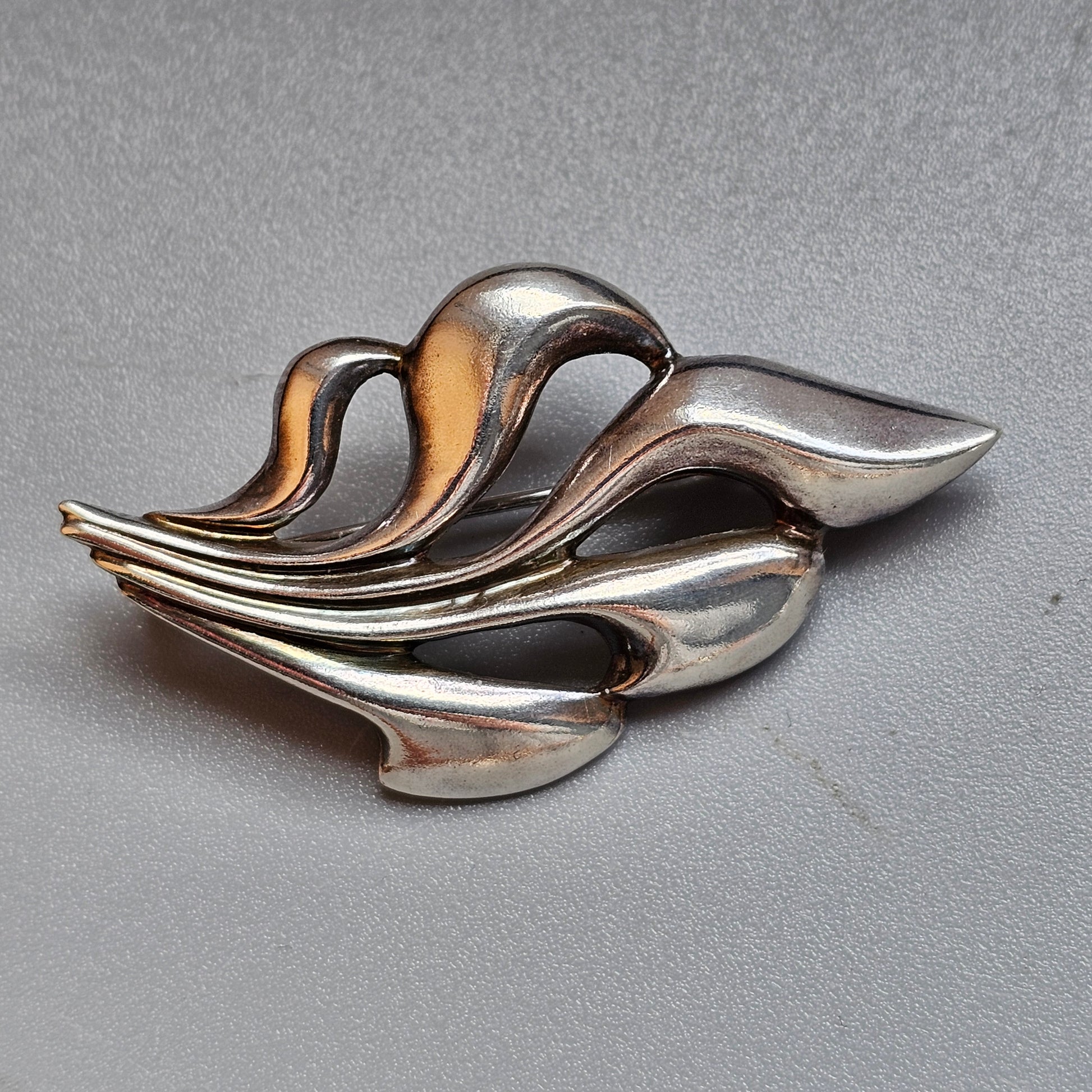 Abstract silver brooch with flowing, curved shapes resembling stylized leaves or waves.