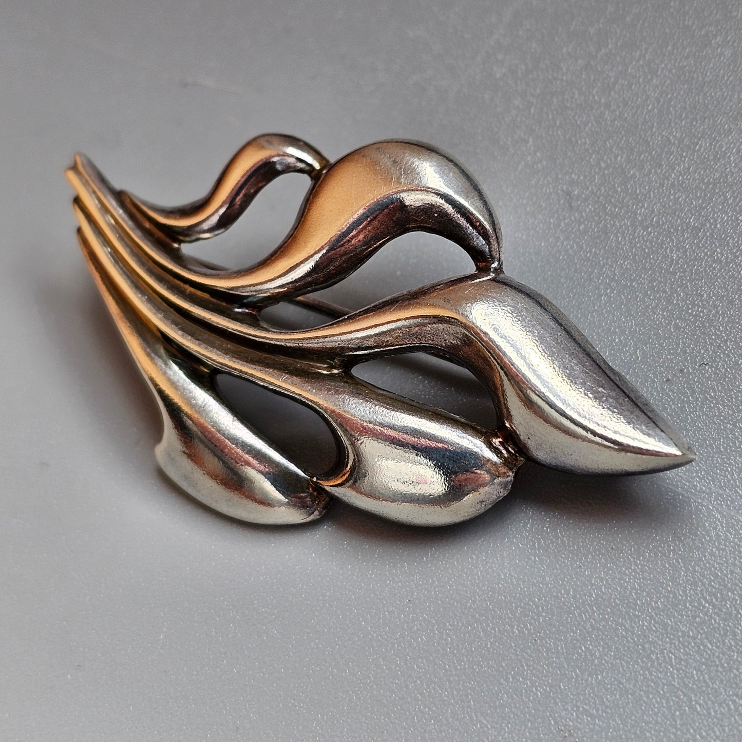 Stylized silver brooch or pin with flowing, organic leaf-like shapes.