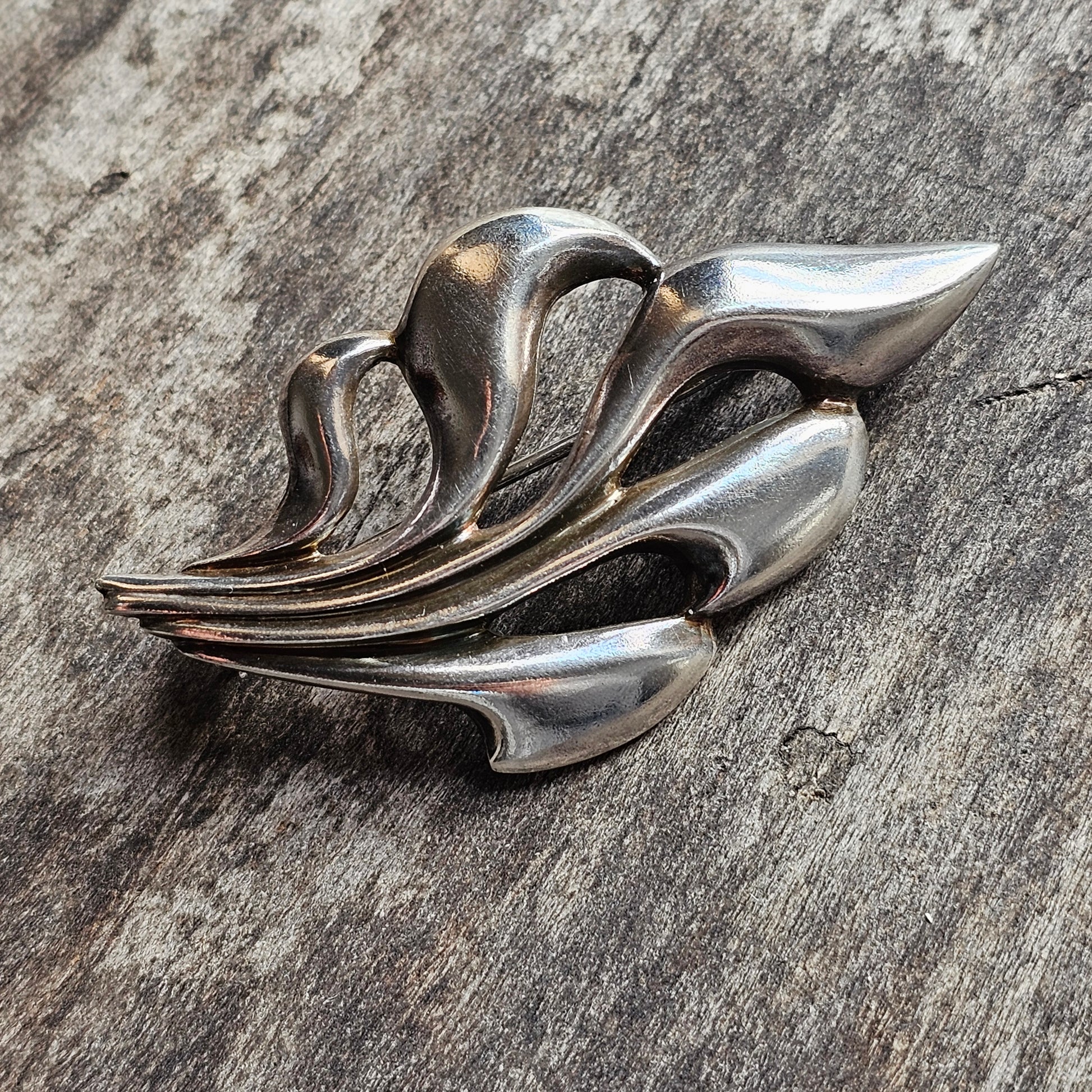 Stylized silver brooch or pin shaped like an abstract leaf or flame.