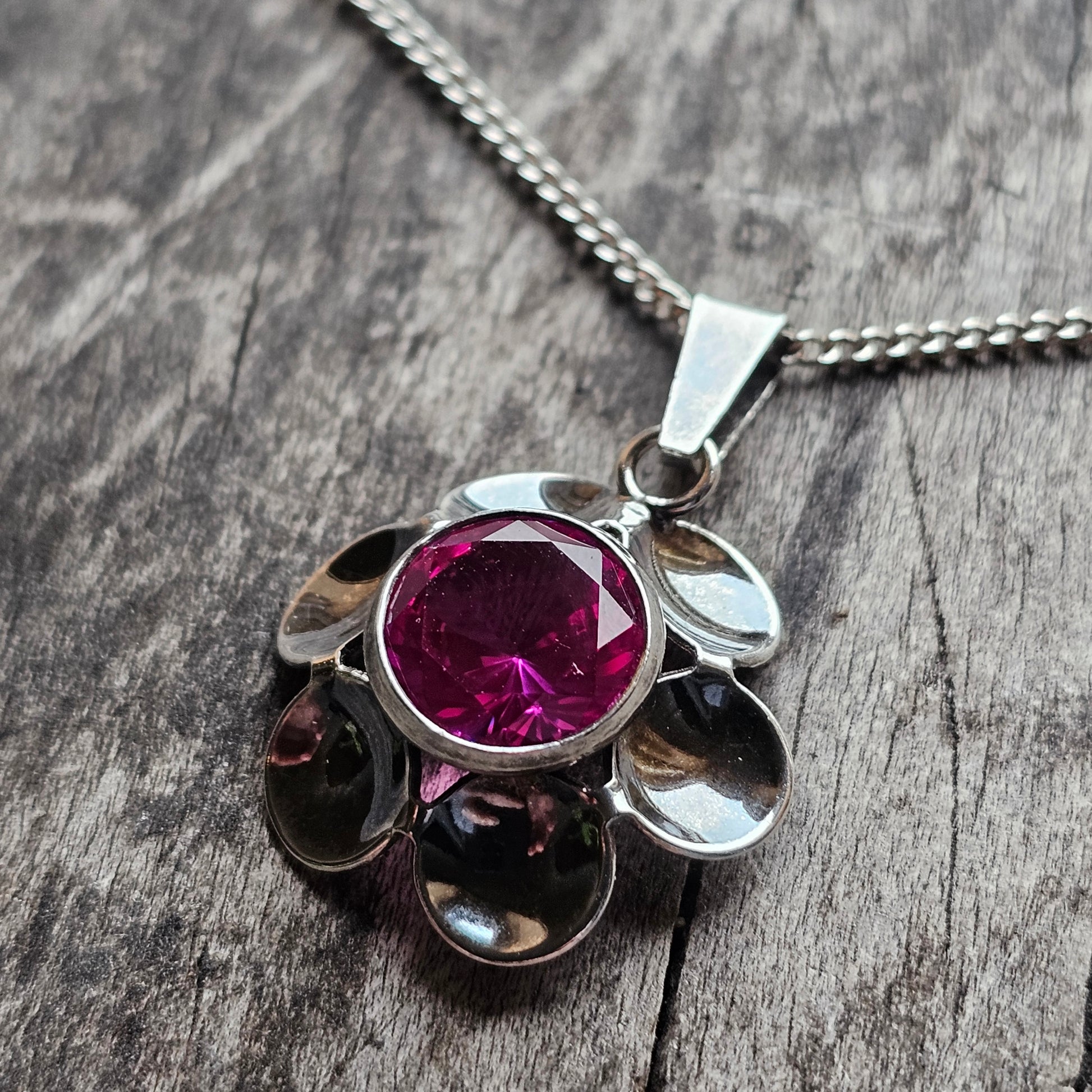 Silver pendant necklace featuring a deep pink gemstone surrounded by petal-like metallic elements.