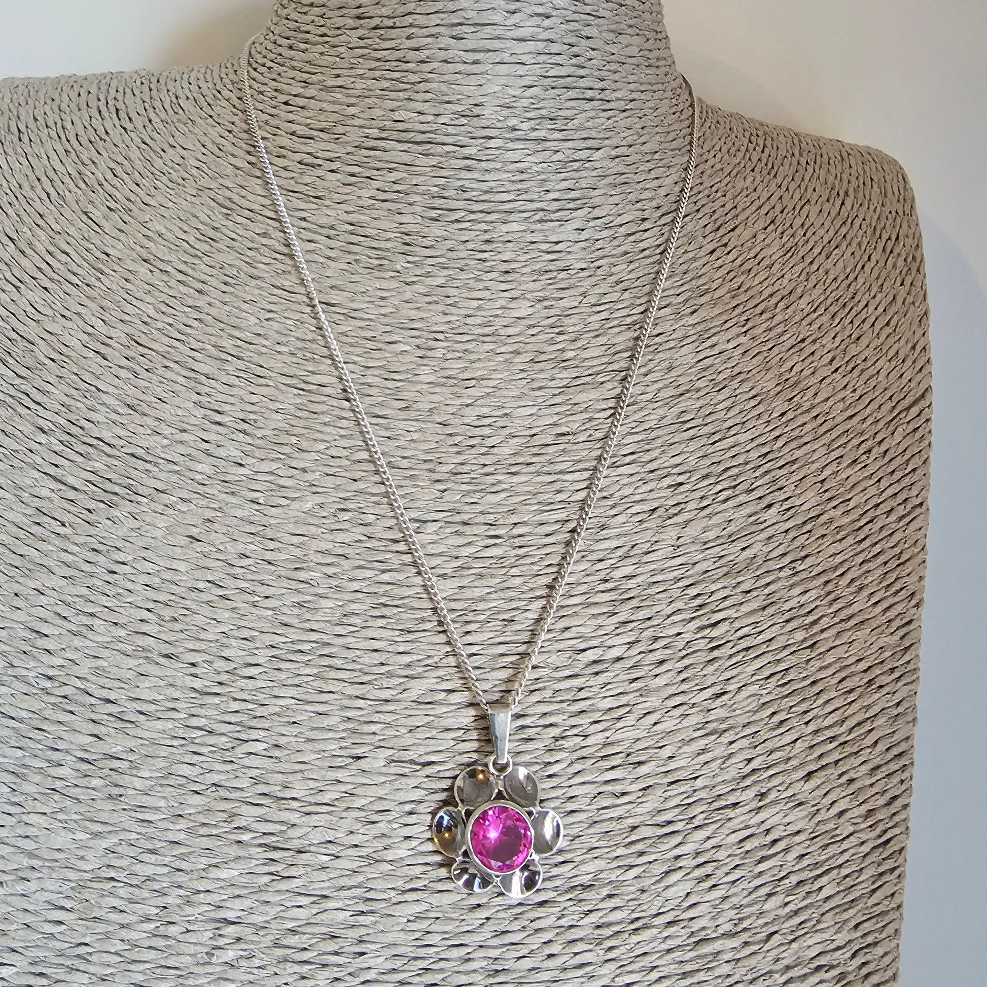 Silver necklace with a pink gemstone pendant shaped like a flower or sun.