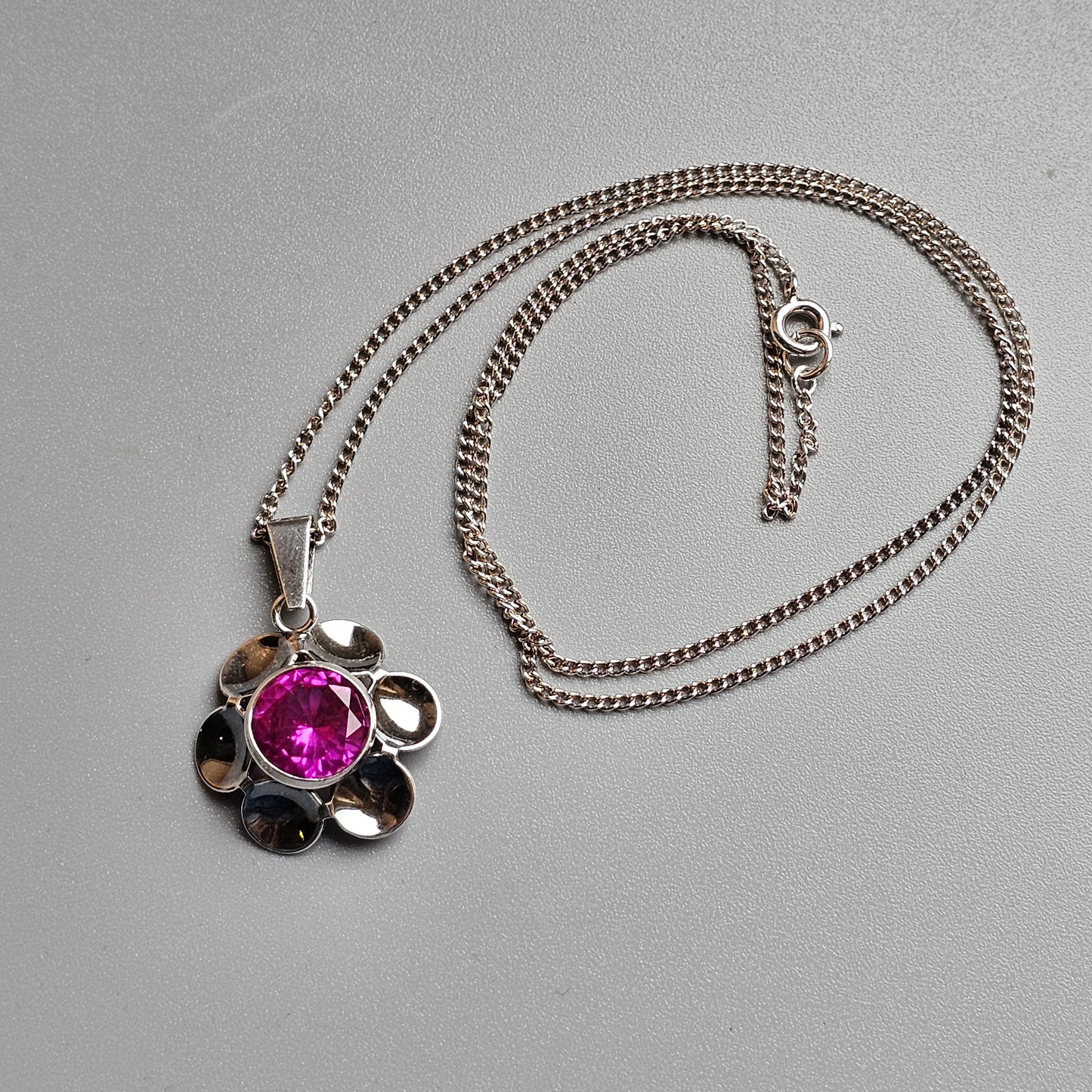 Silver flower-shaped pendant necklace with a pink gemstone center.