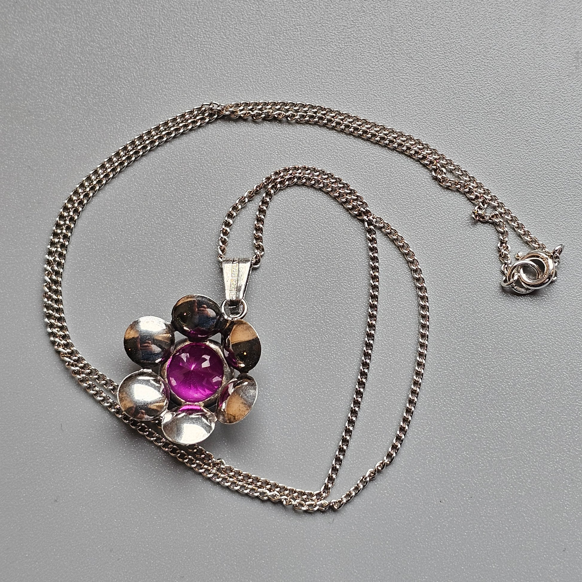 Flower-shaped pendant necklace with a central pink gemstone surrounded by metallic petals on a silver chain.