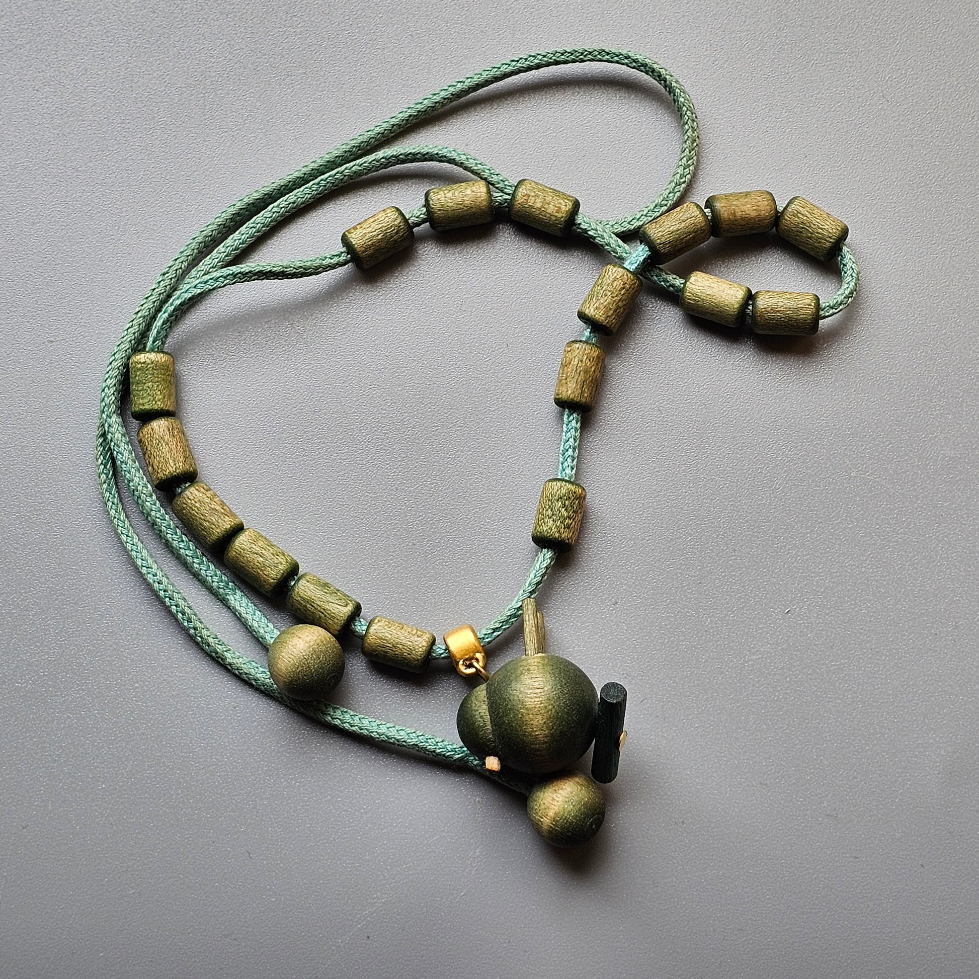 Necklace made of green cord and wooden beads with a spherical pendant.