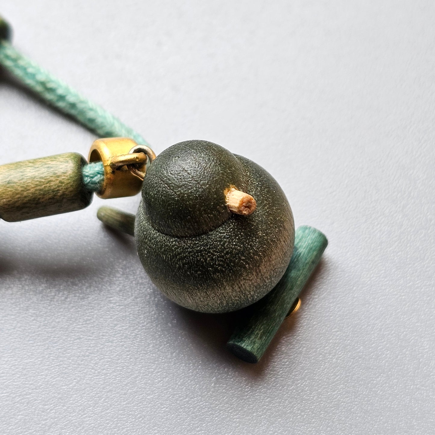 Dark green spherical bead with a textured surface, attached to a cord.