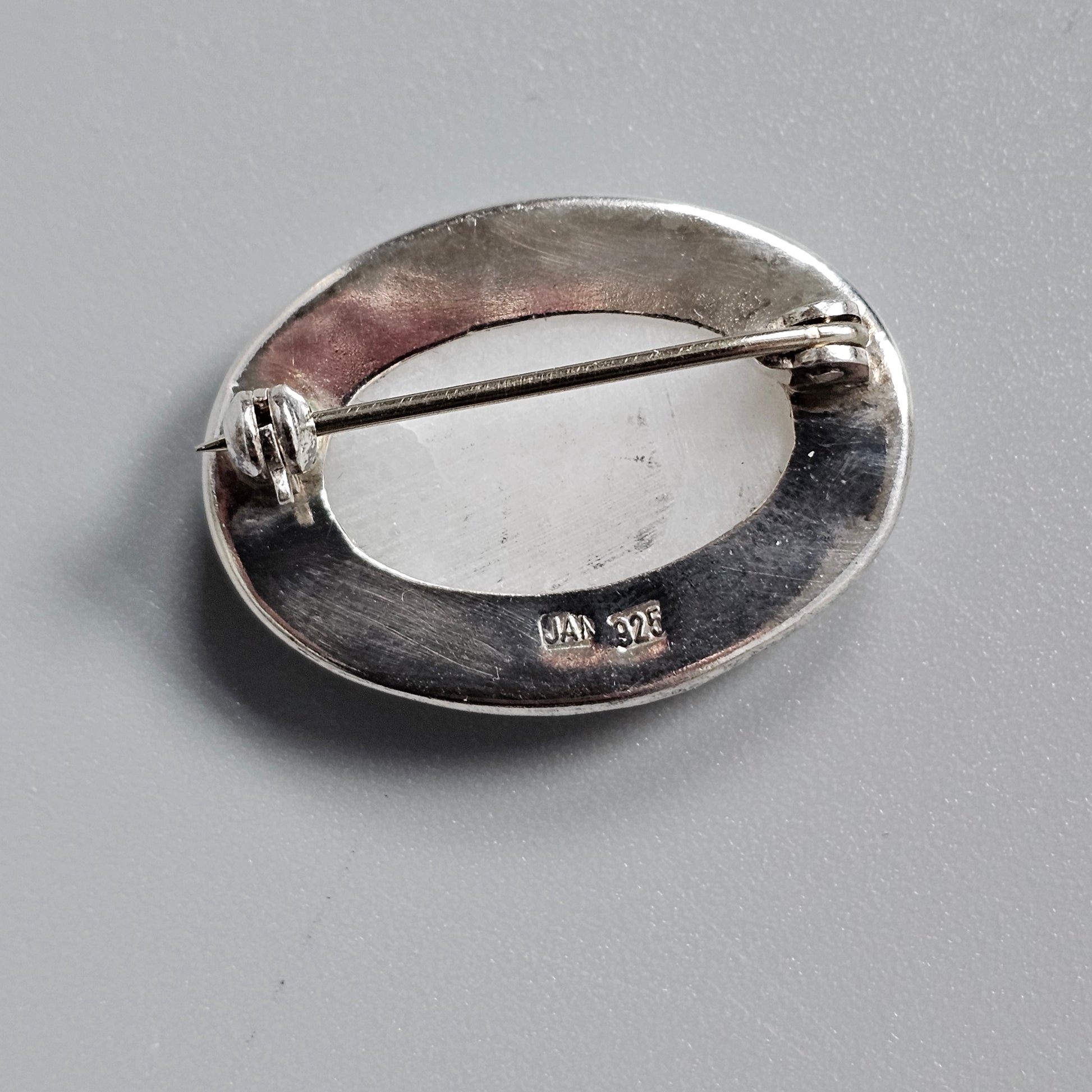 Oval-shaped silver brooch with a pin clasp on the back.