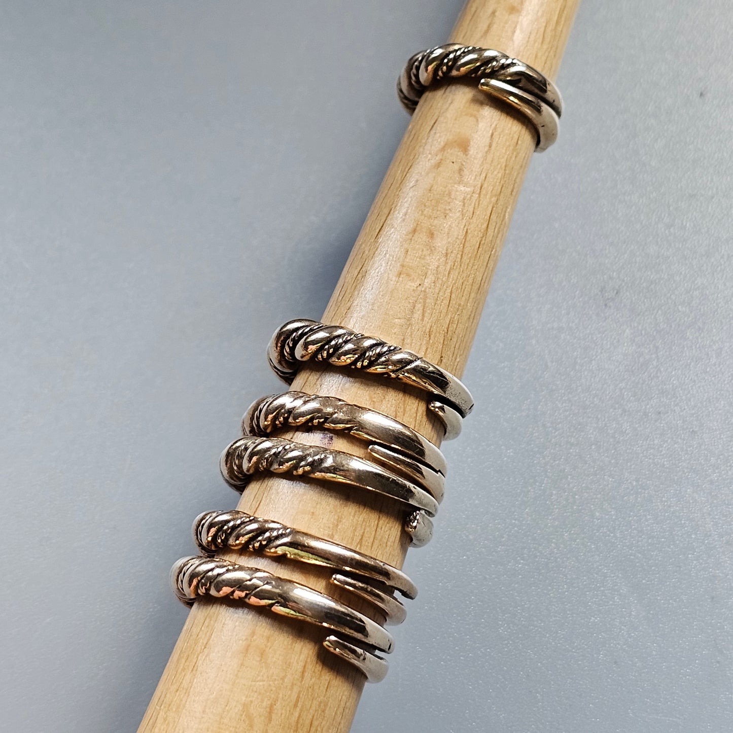 Twisted silver rings stacked on a wooden dowel or rod.