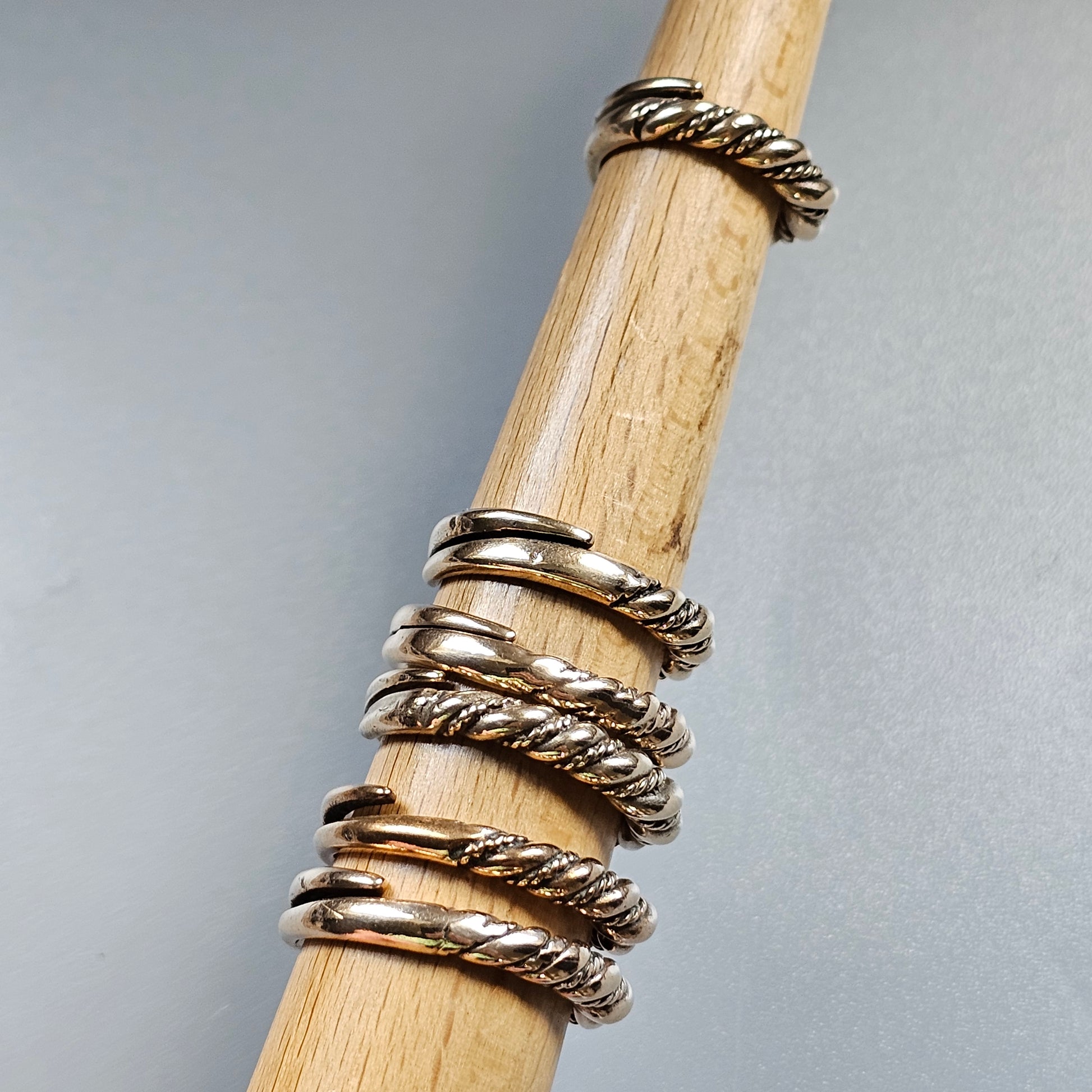 Stack of silver twisted and plain metal rings on a wooden dowel.