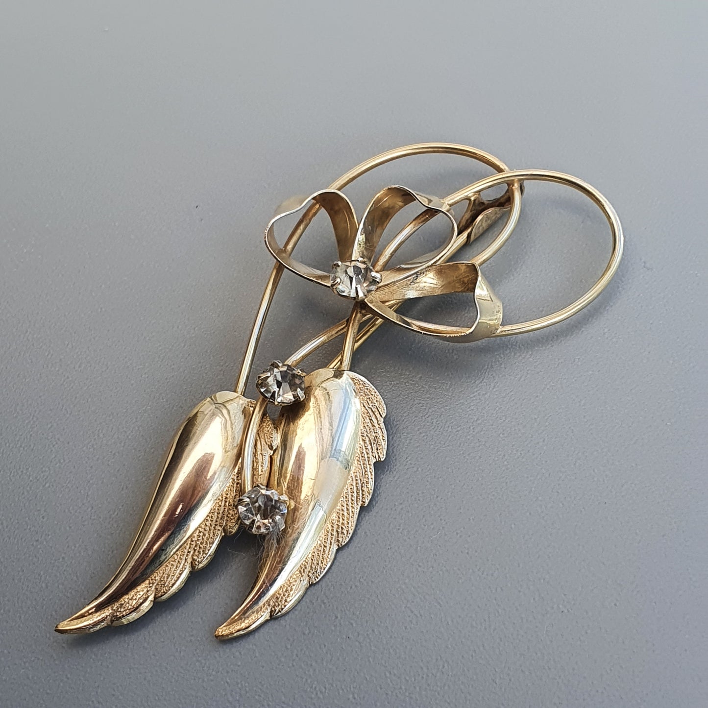 Gold-toned brooch featuring a bow design with dangling leaf or wing-like elements and small gemstones.