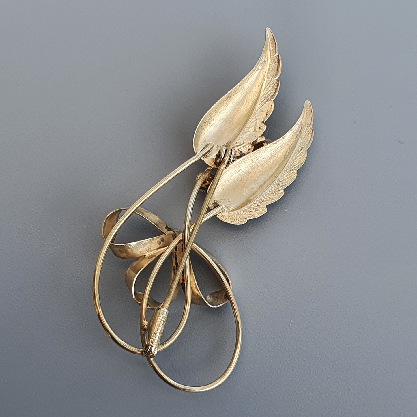 Gold-toned leaf-shaped brooch with curving stems and delicate details.