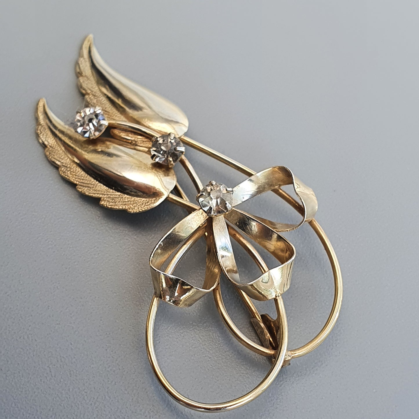 Gold-toned brooch featuring wings, a bow, and rhinestones in a floral design.