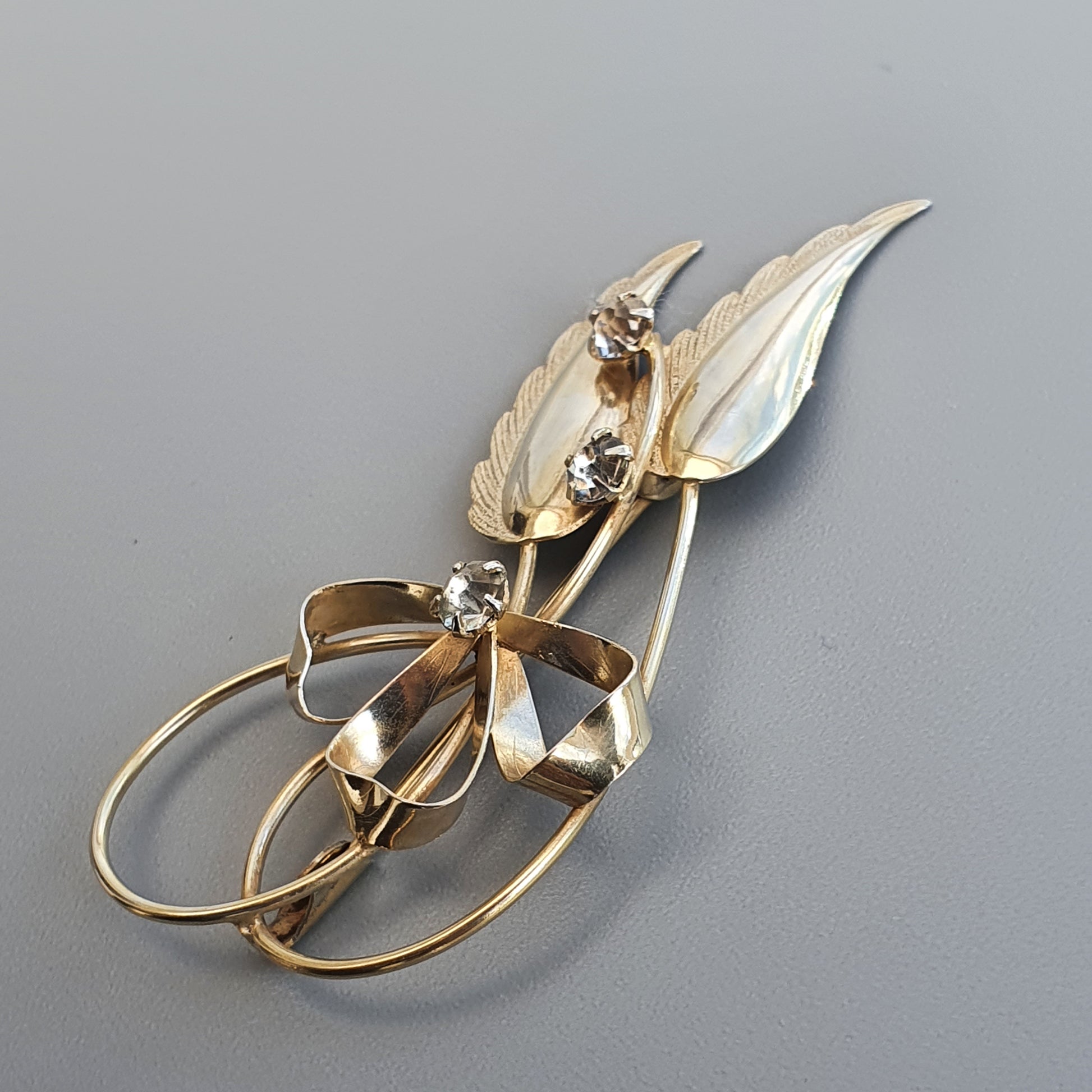 Gold-toned floral brooch with leaf shapes and diamond accents.