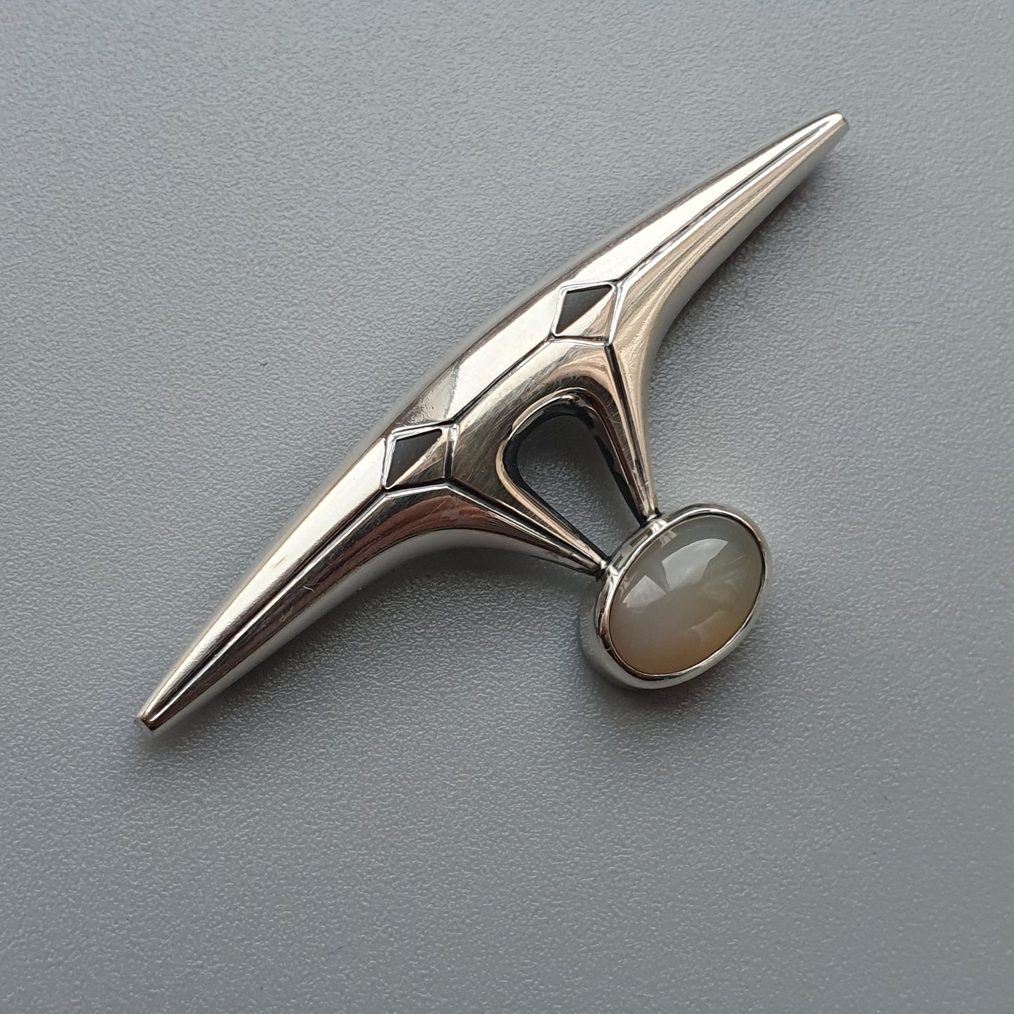 Sleek silver brooch with a pointed shape and an oval gemstone accent.