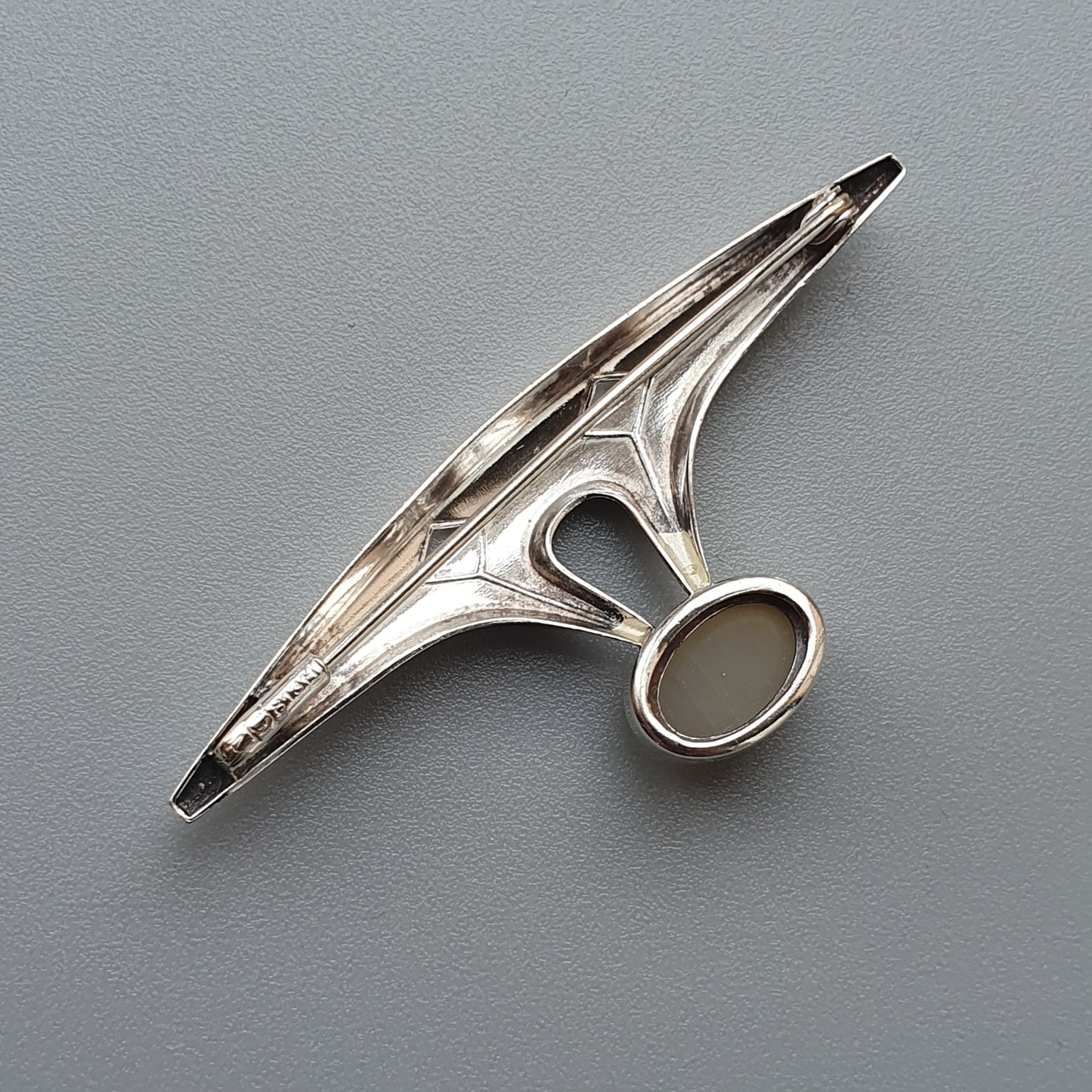 Sleek, futuristic-looking silver brooch or pin with an elongated wing-like shape and circular element.