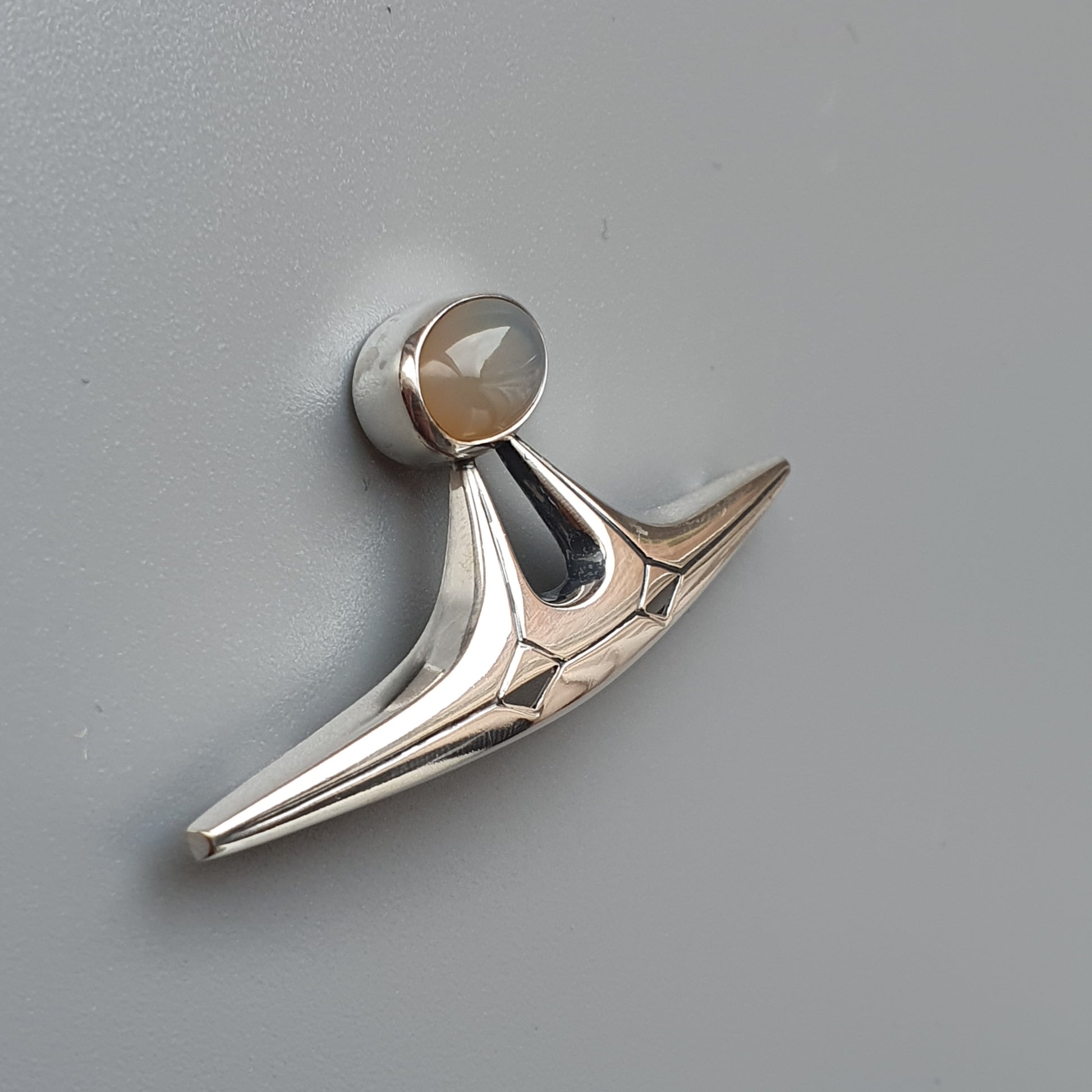 Sleek, metallic hood ornament or car emblem with a pointed, wing-like shape.