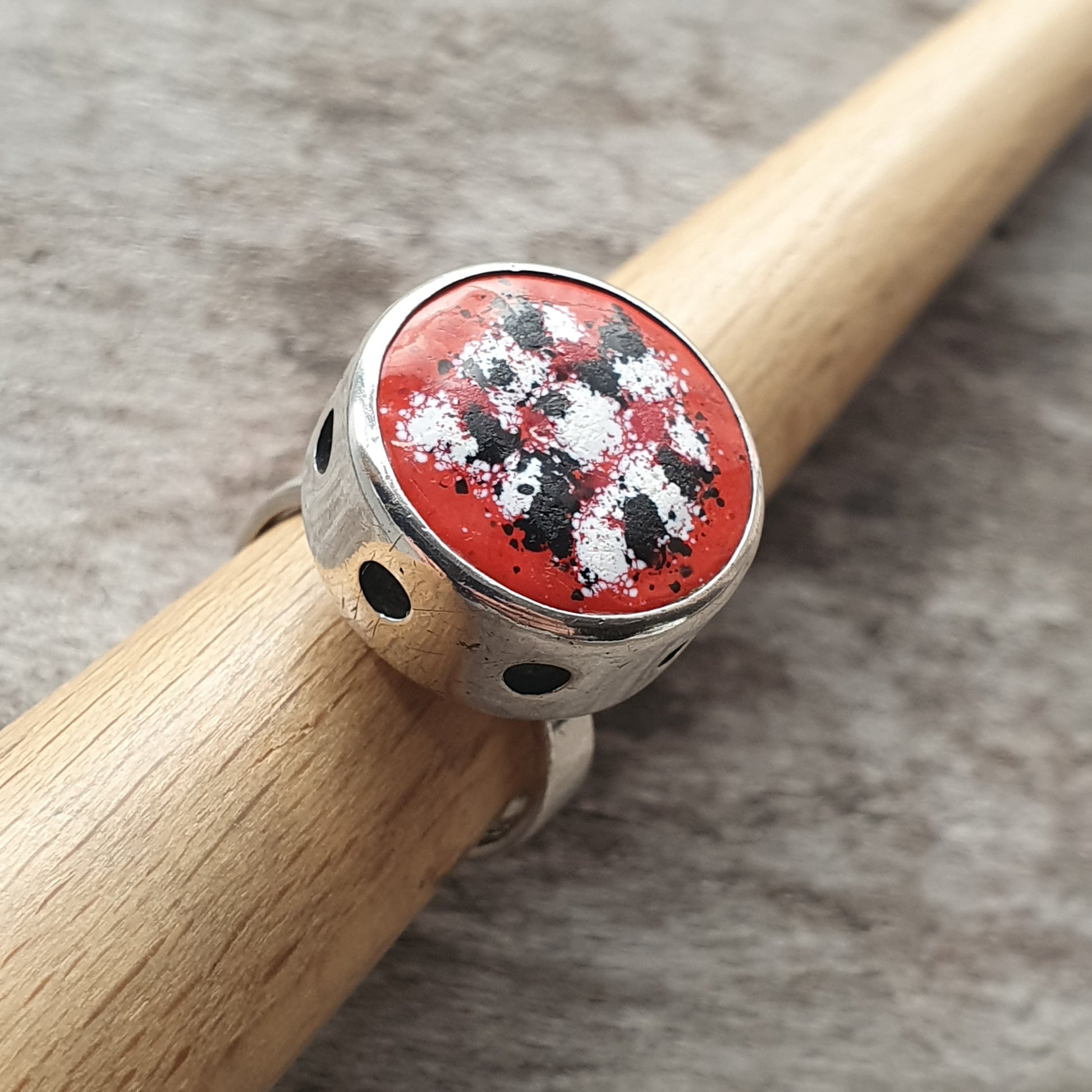 Silver ring with a red, black, and white patterned oval stone or enamel centerpiece.