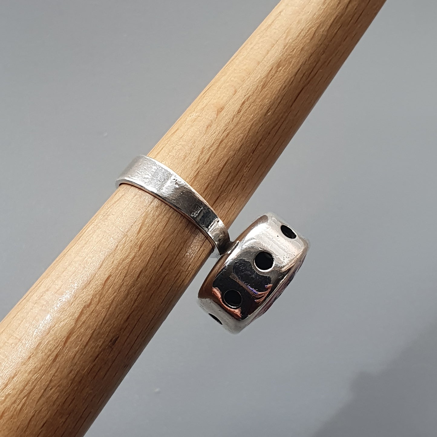 Silver ring with circular cutout patterns wrapped around a wooden dowel.