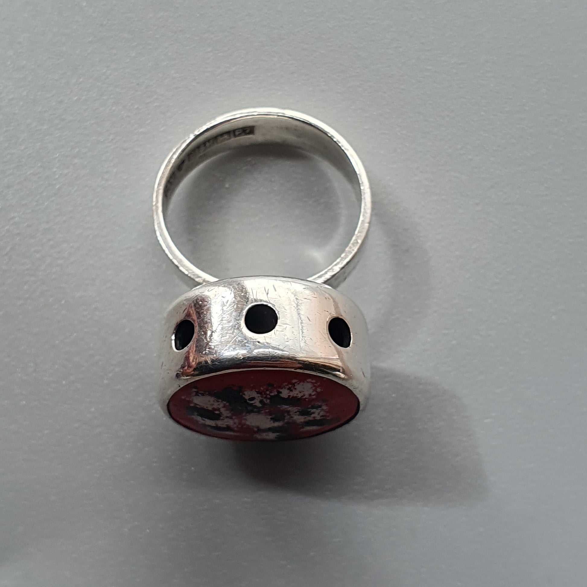 Silver ring with a red circular top featuring small holes.