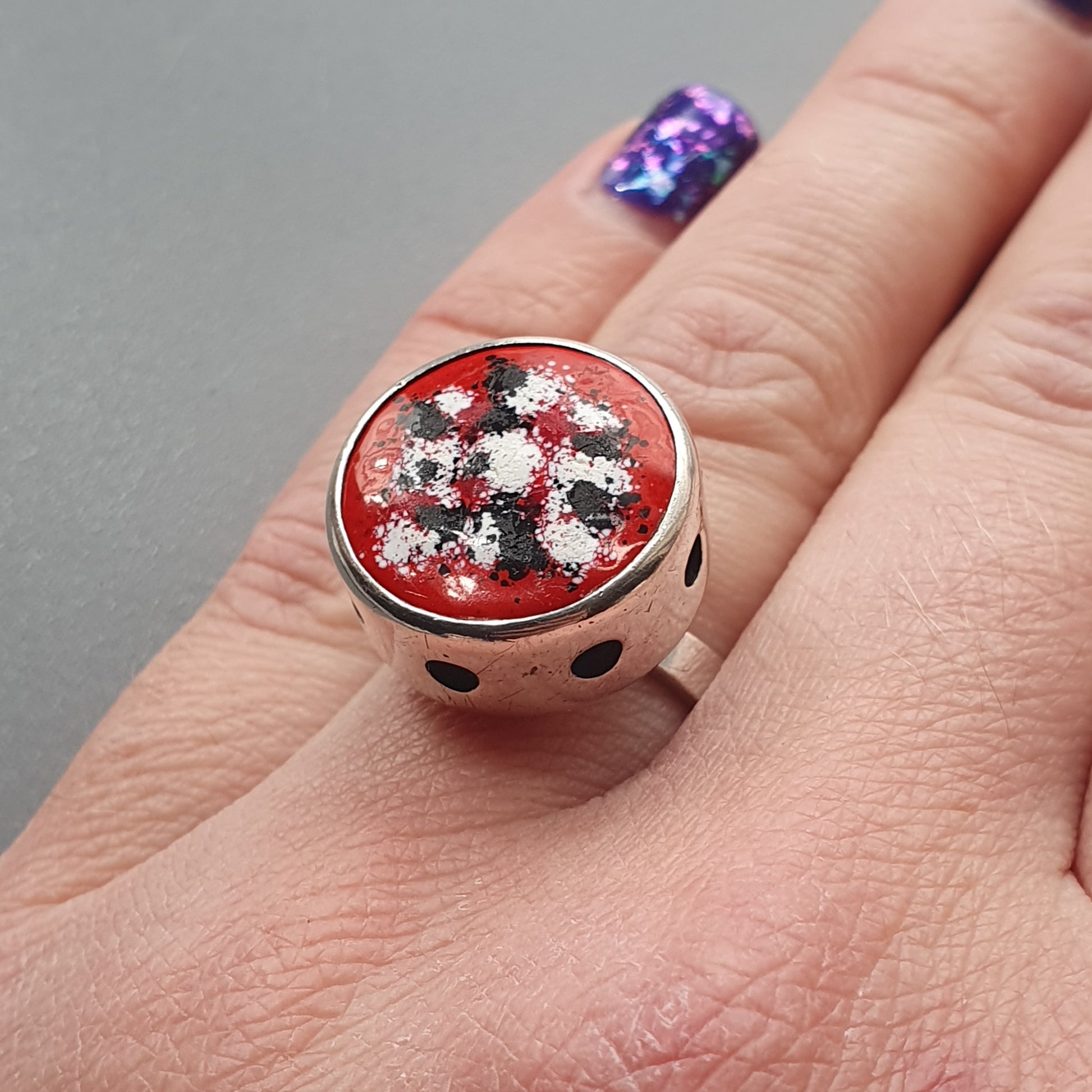 Decorative ring with a red, white, and black floral design in a circular setting.