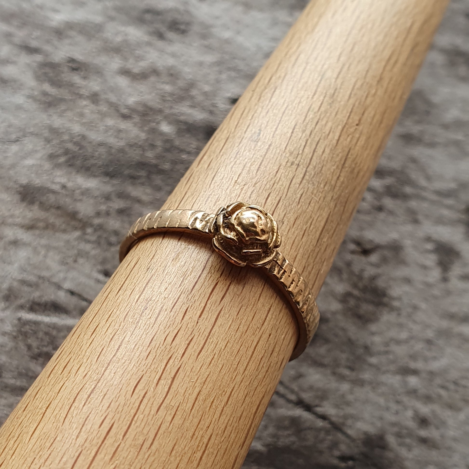 Gold ring with a small rose-shaped design on top.