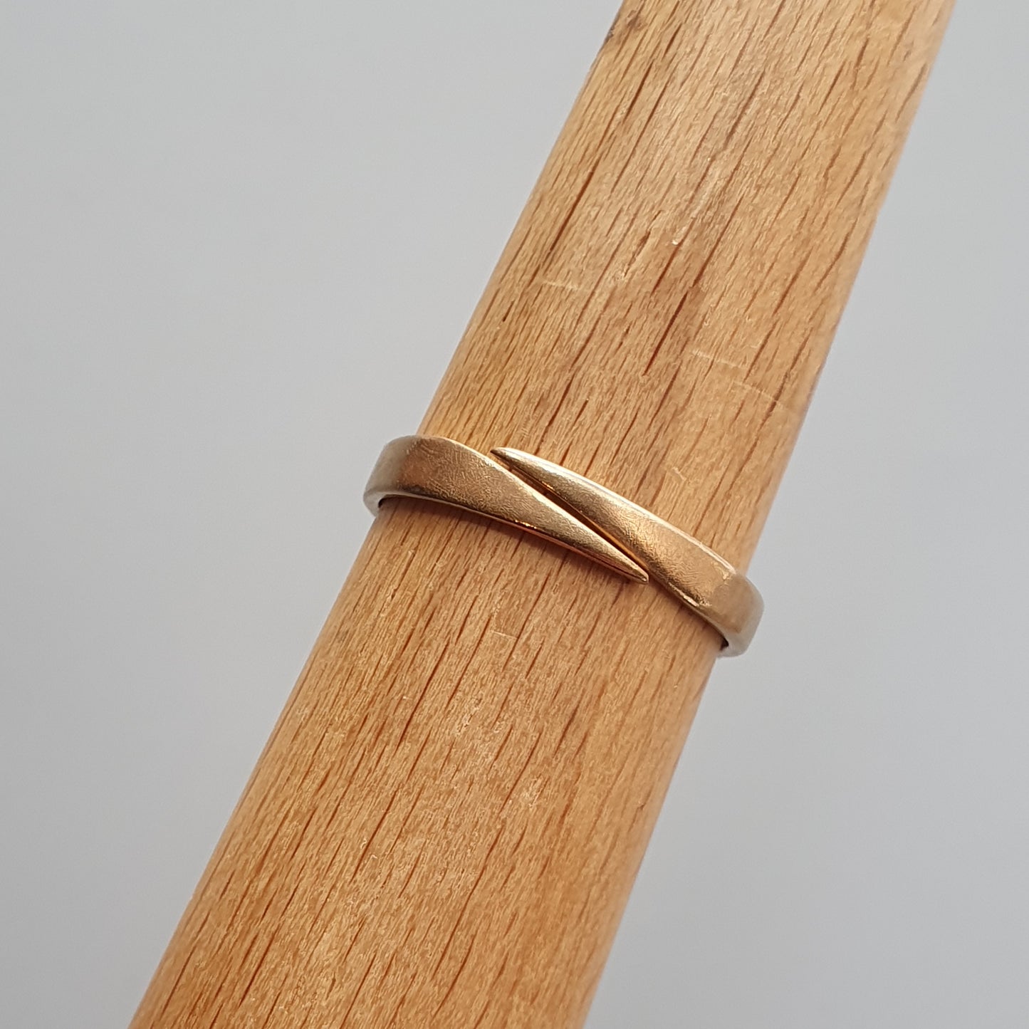 Gold ring with a twisted or overlapping design on a wooden surface.