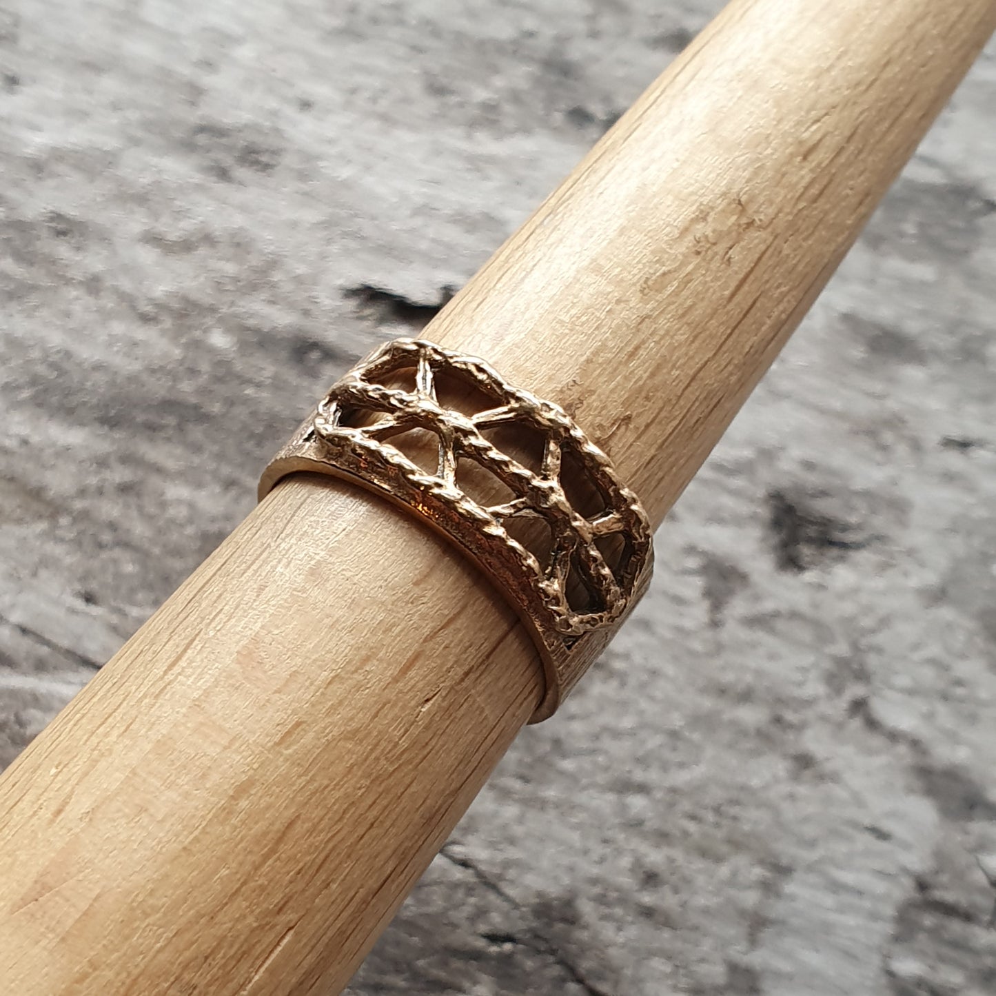 Textured gold ring with an intricate lattice-like pattern wrapped around a wooden dowel.