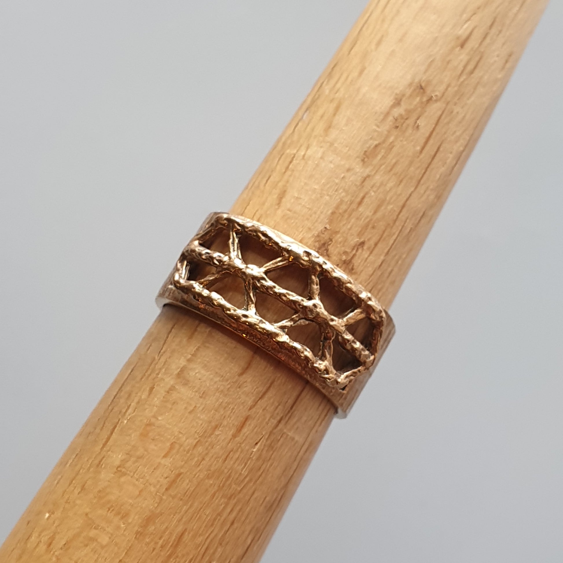 Gold ring with a criss-cross pattern wrapped around a wooden dowel.