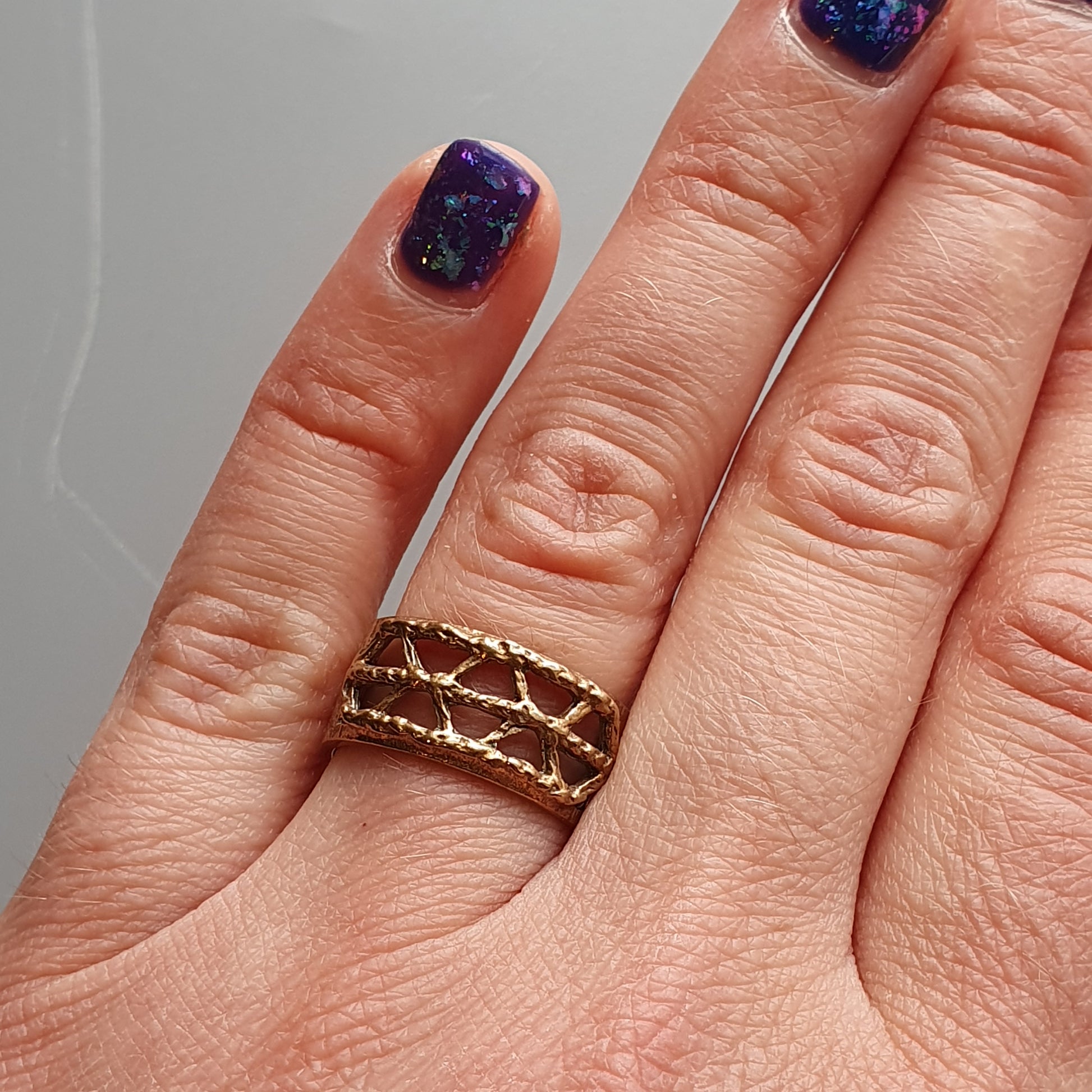 Gold ring with a lattice or criss-cross pattern worn on a finger.