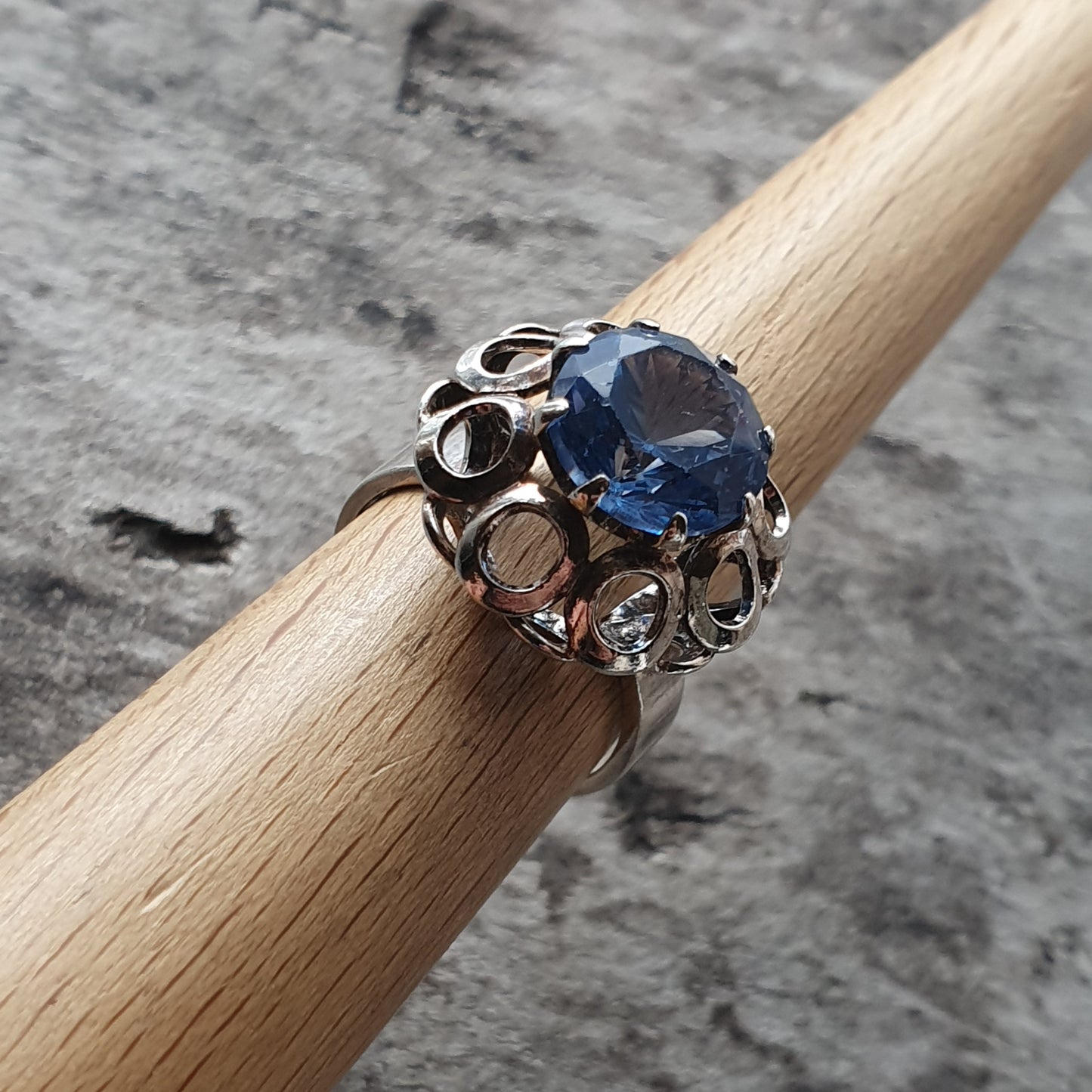 Silver ring with an ornate setting featuring a round blue gemstone.