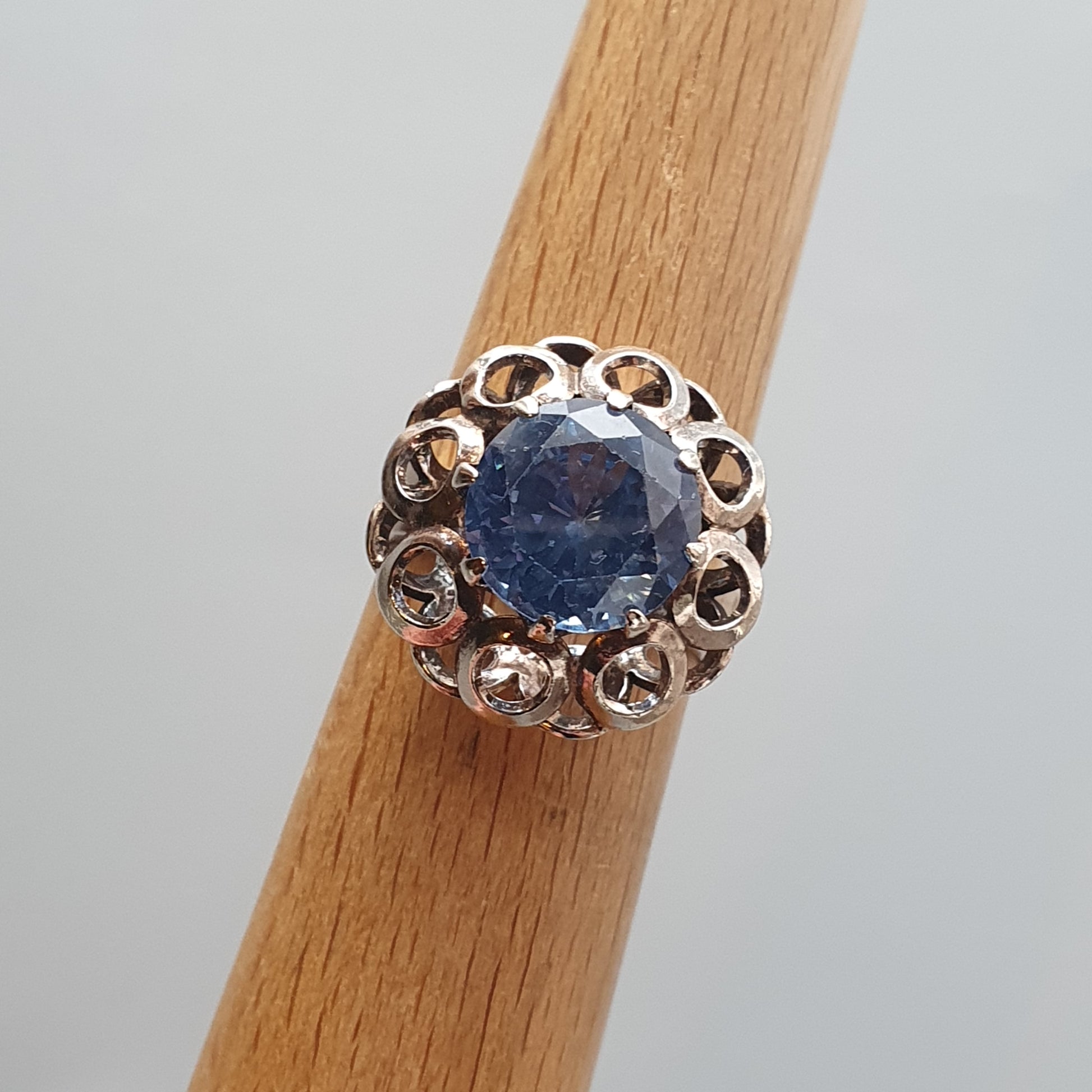 Ornate silver ring with a central blue gemstone surrounded by smaller clear stones.