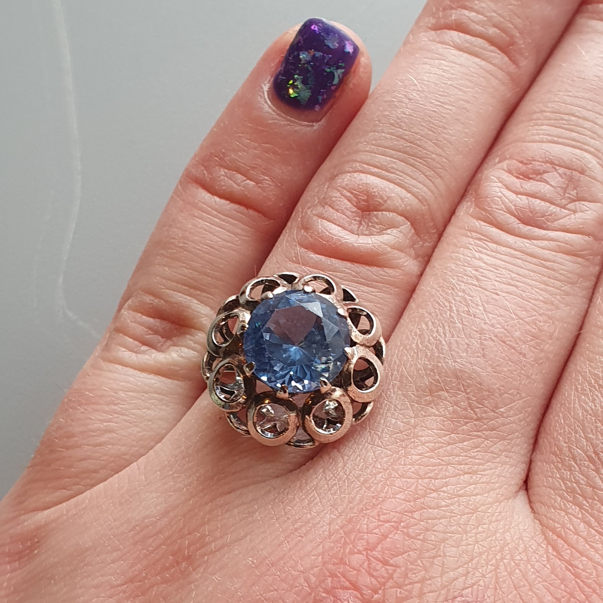 Ornate gold ring with a prominent blue gemstone in an intricate floral-like setting.