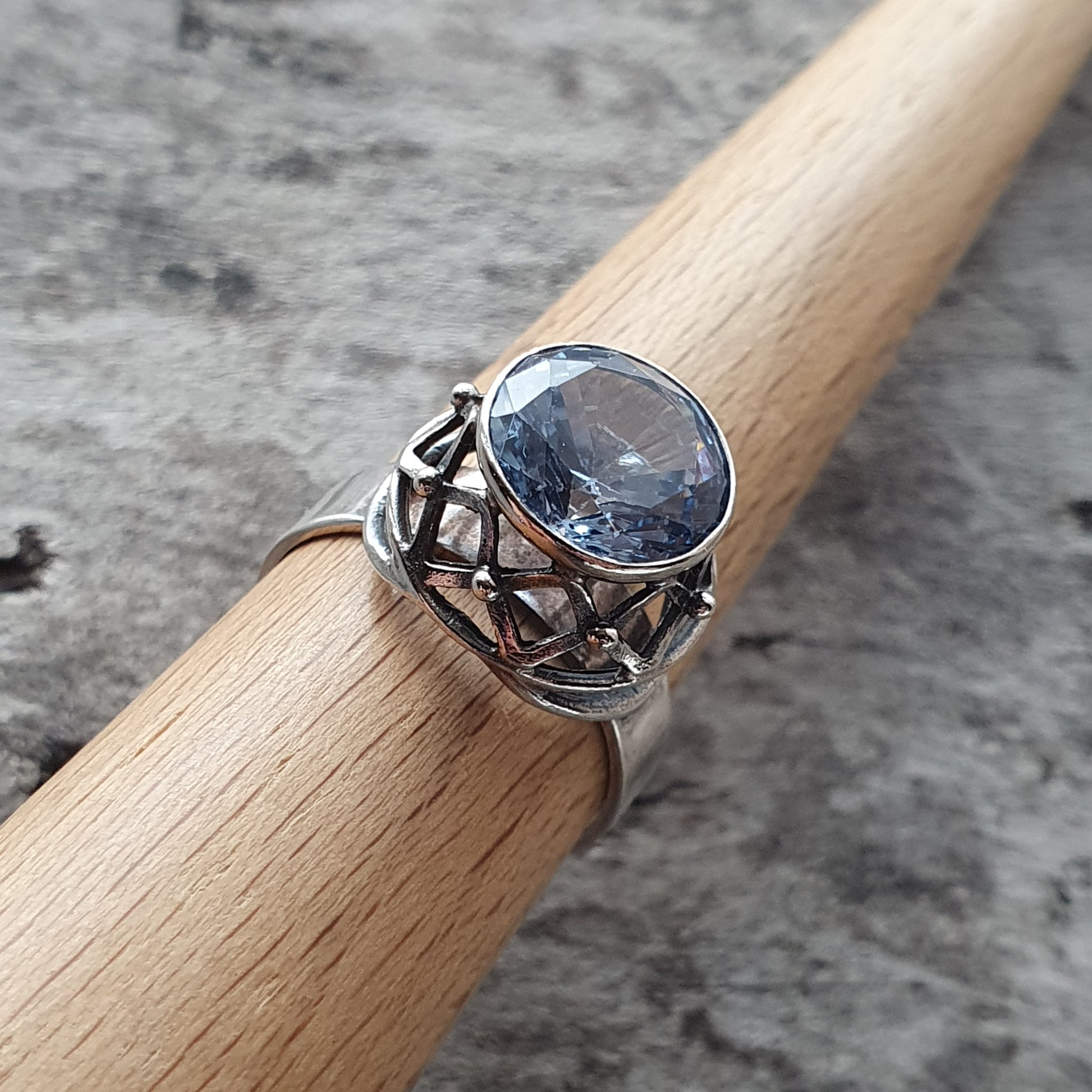 Silver ring with an oval light blue gemstone and intricate metalwork on the band.