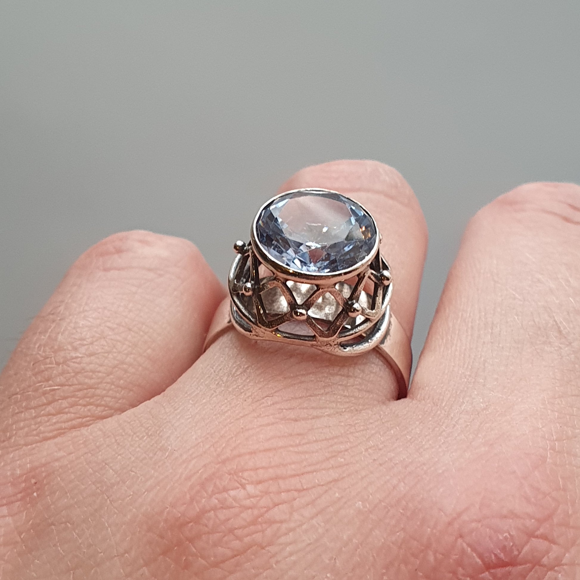 Ornate silver ring featuring a round light blue gemstone in an intricate setting.