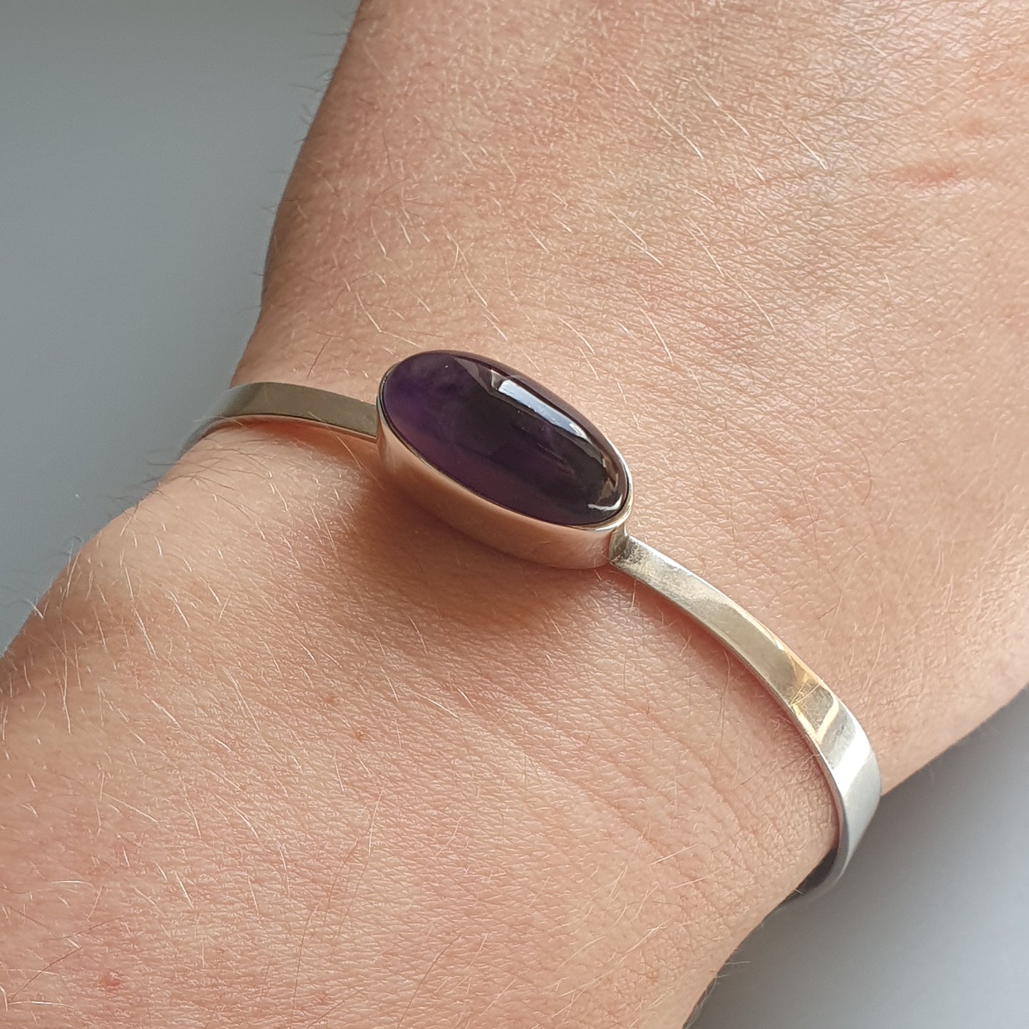 Silver bracelet with an oval purple gemstone.