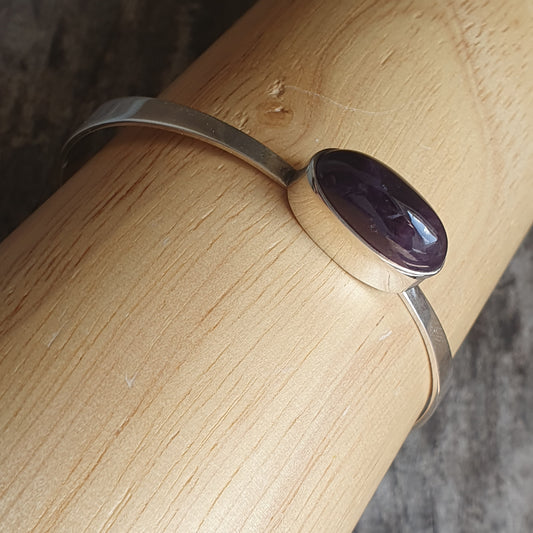 Silver bracelet with a single oval purple gemstone.