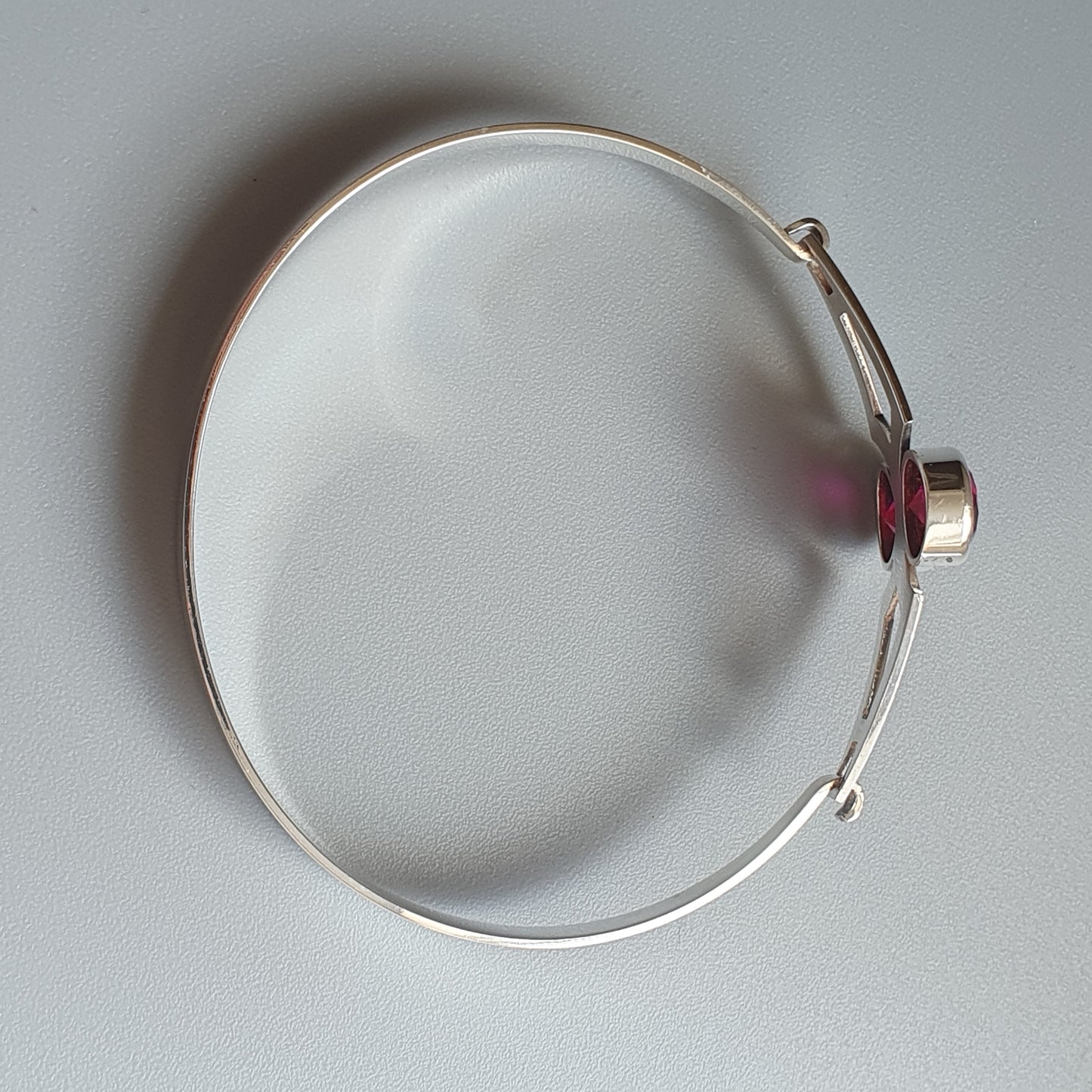 Silver adjustable bangle bracelet with a small pink gemstone or bead accent.