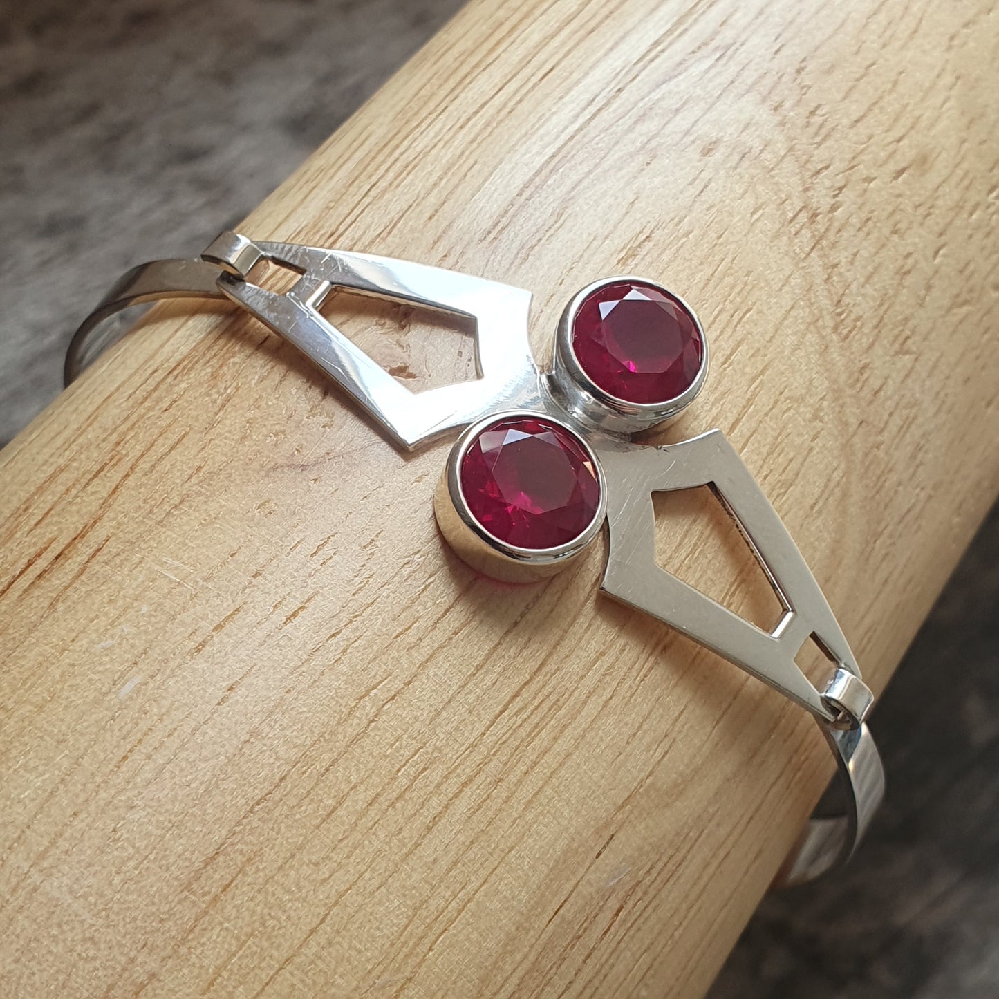 Silver bracelet with two red gemstones set in geometric shapes.