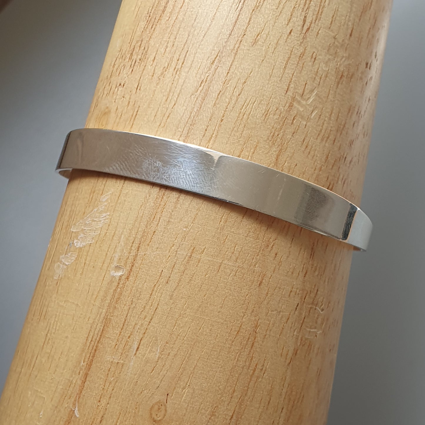 Simple silver metal band or ring wrapped around a wooden cylinder.