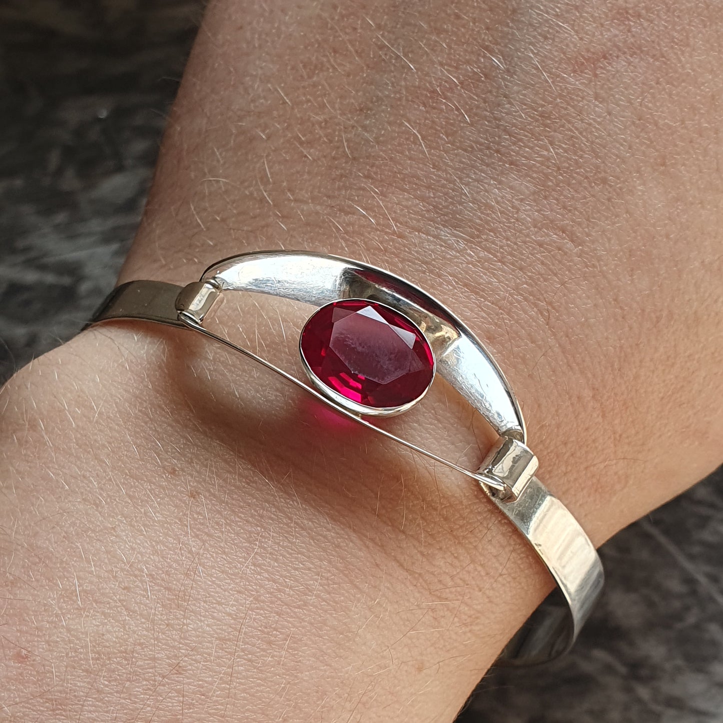 Silver bracelet with an oval red gemstone set in the center.