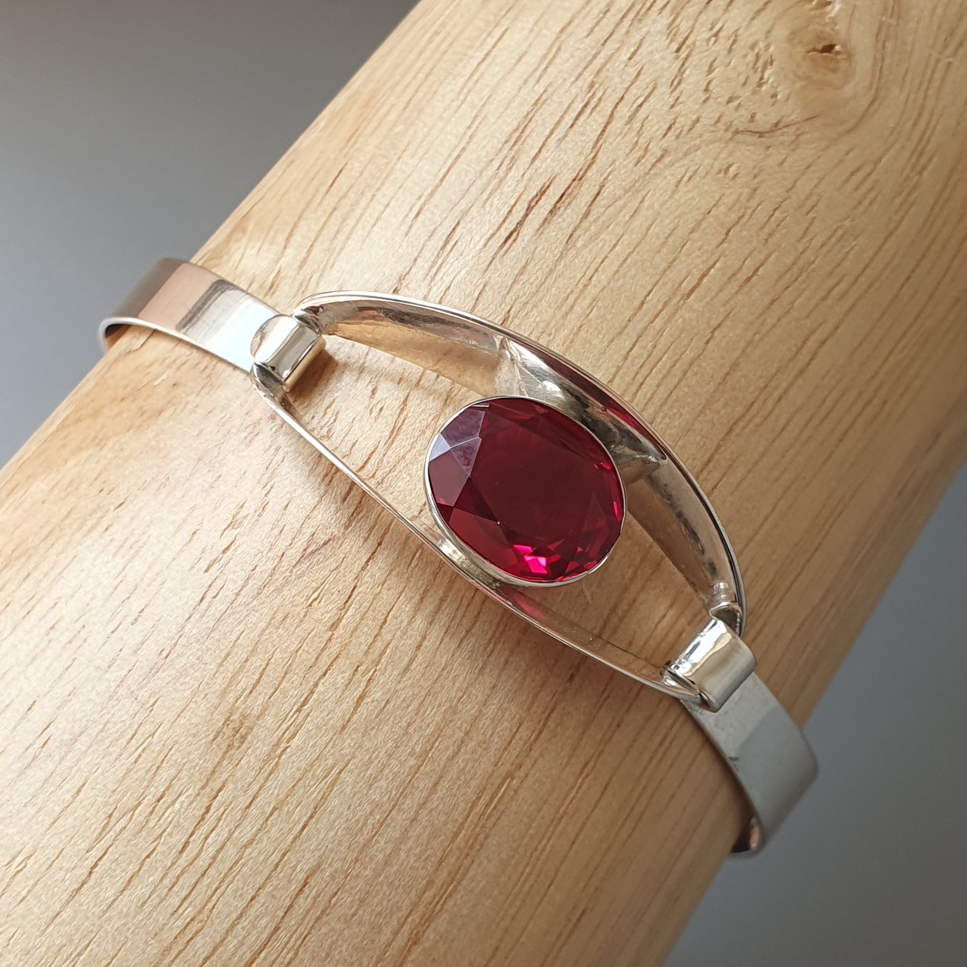 Silver bracelet featuring a single oval-cut red gemstone.